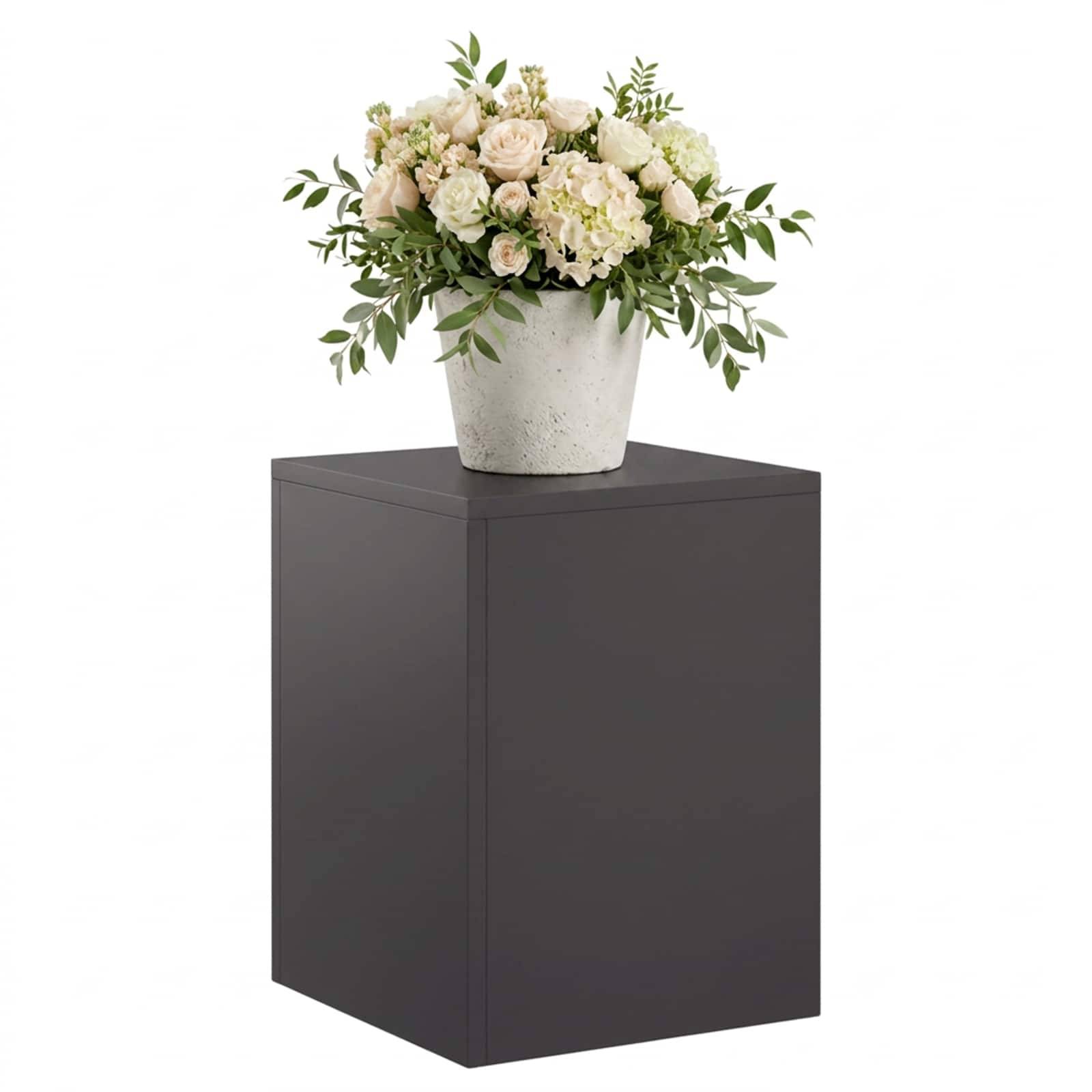 Weiße Blumengestaltung in einer Vase, präsentiert auf einem dunklen Sockelständer vor einem einfachen weißen Hintergrund.