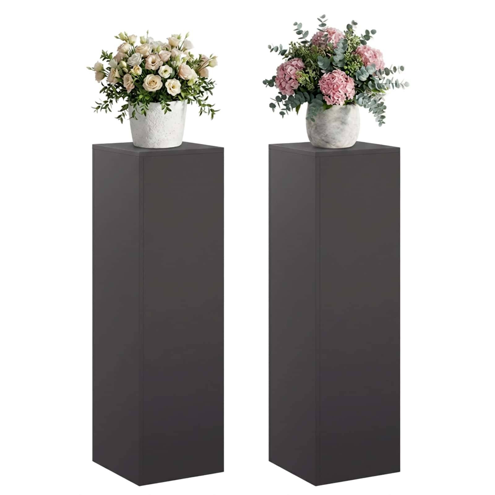 Zwei Blumenarrangements in weißen Töpfen stehen auf hohen dunklen Sockeln vor einem weißen Hintergrund.
