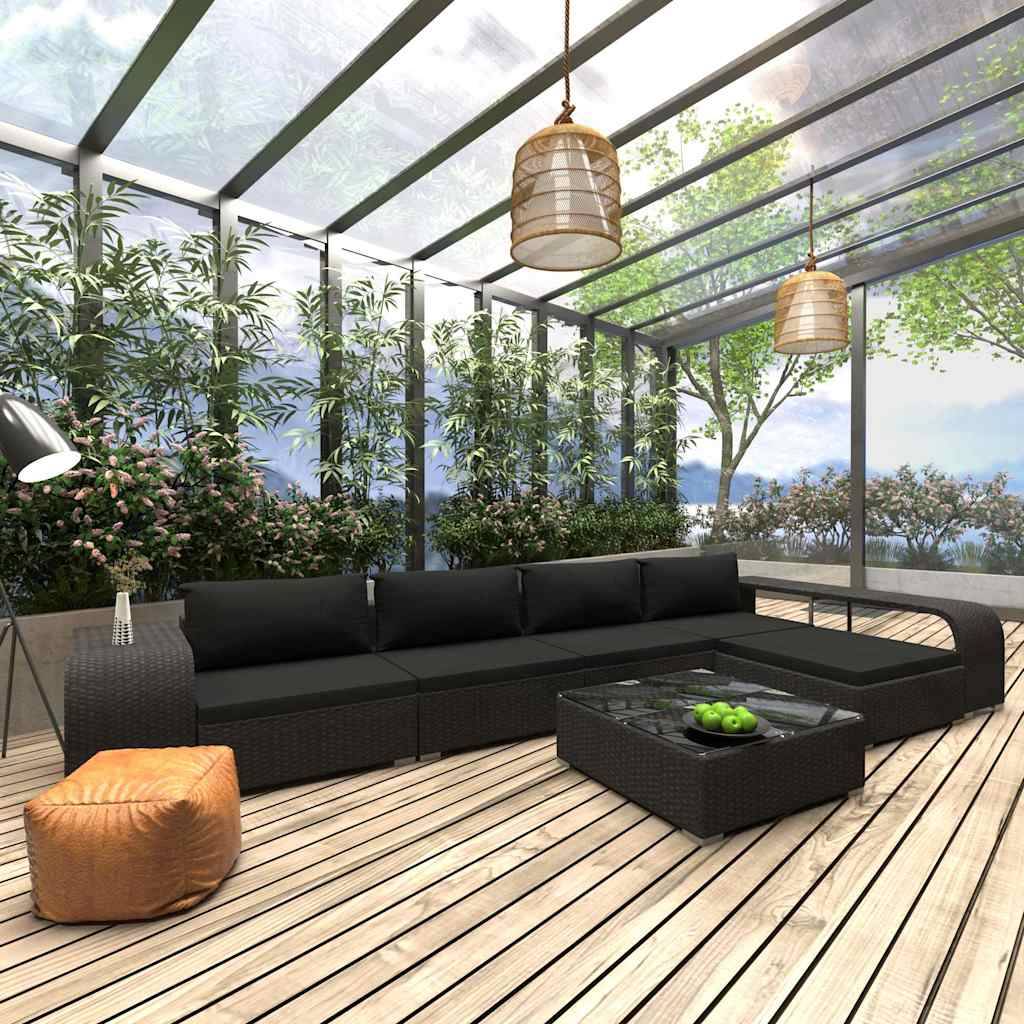 Helles Indoor-Outdoor-Lounge mit schwarzem Ecksofa, niedrigem Couchtisch mit grünen Äpfeln, orangefarbenem Pouf und raumhohen Glaswänden mit Blick auf einen üppigen Garten.