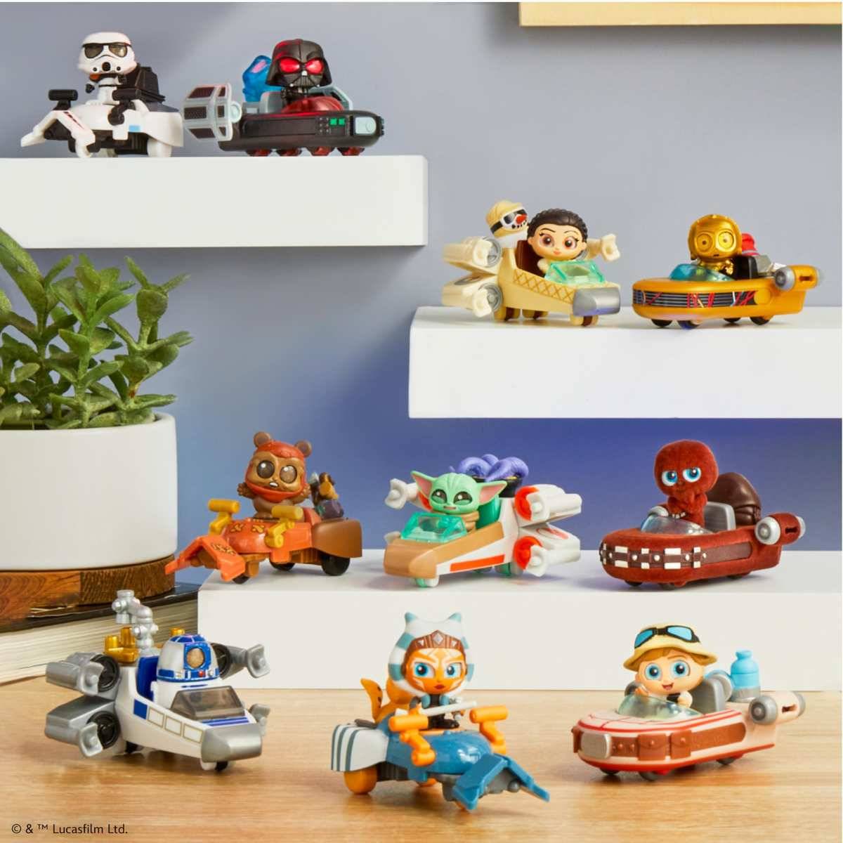 Gemischte Star-Wars-LEGO-Minifiguren in kleinen Fahrzeugen, die auf weißen Regalen vor einer grauen Wand ausgestellt sind, mit einer Topfpflanze auf der linken Seite.