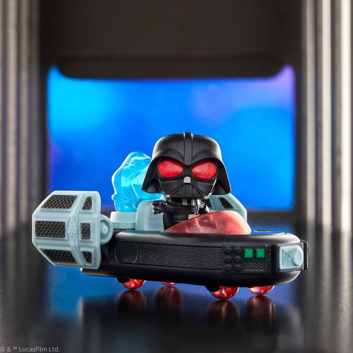 Spielzeug-Figur des Darth Vader, der in einem kleinen schwarzen Raumschiff mit roten Akzenten und blauem Motorenschein vor einem blau beleuchteten Hintergrund fährt.