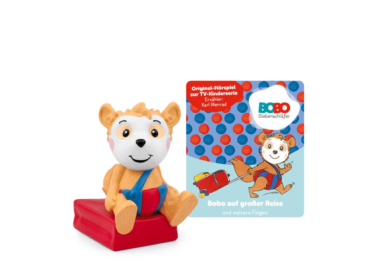 Ein kuscheliger Bobo-Bär sitzt auf einem roten Koffer neben einem 