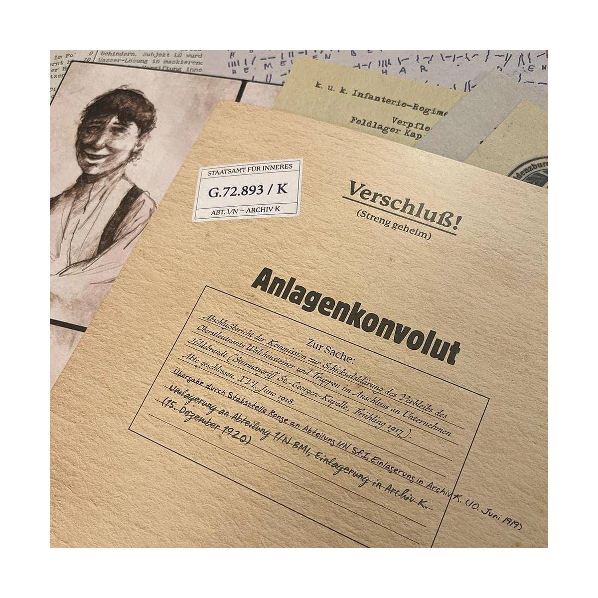 Nahaufnahme von Archivordnern und Papieren mit deutschen Beschriftungen, einschließlich 'Anlagenkonvolut' und 'Verschluß!', mit einer teilweise sichtbaren Porträtskizze.