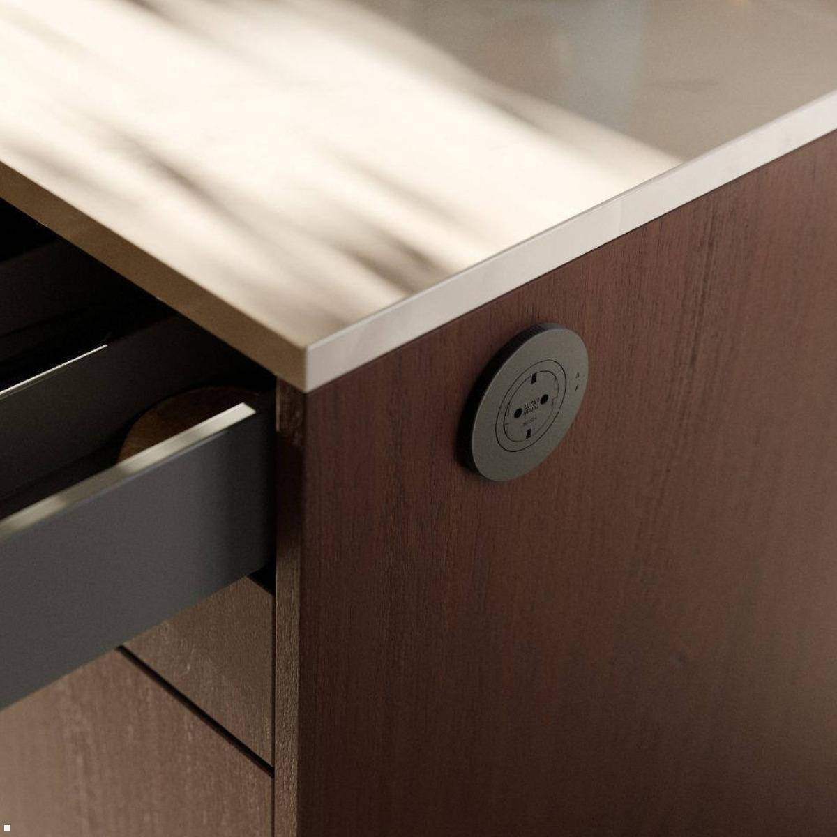 Nahaufnahme einer Ecke eines Holzschranks mit einer gebürsteten Metalloberseite und einer offenen Schublade; eine runde eingebaute Steckdose ist auf der Seite montiert.