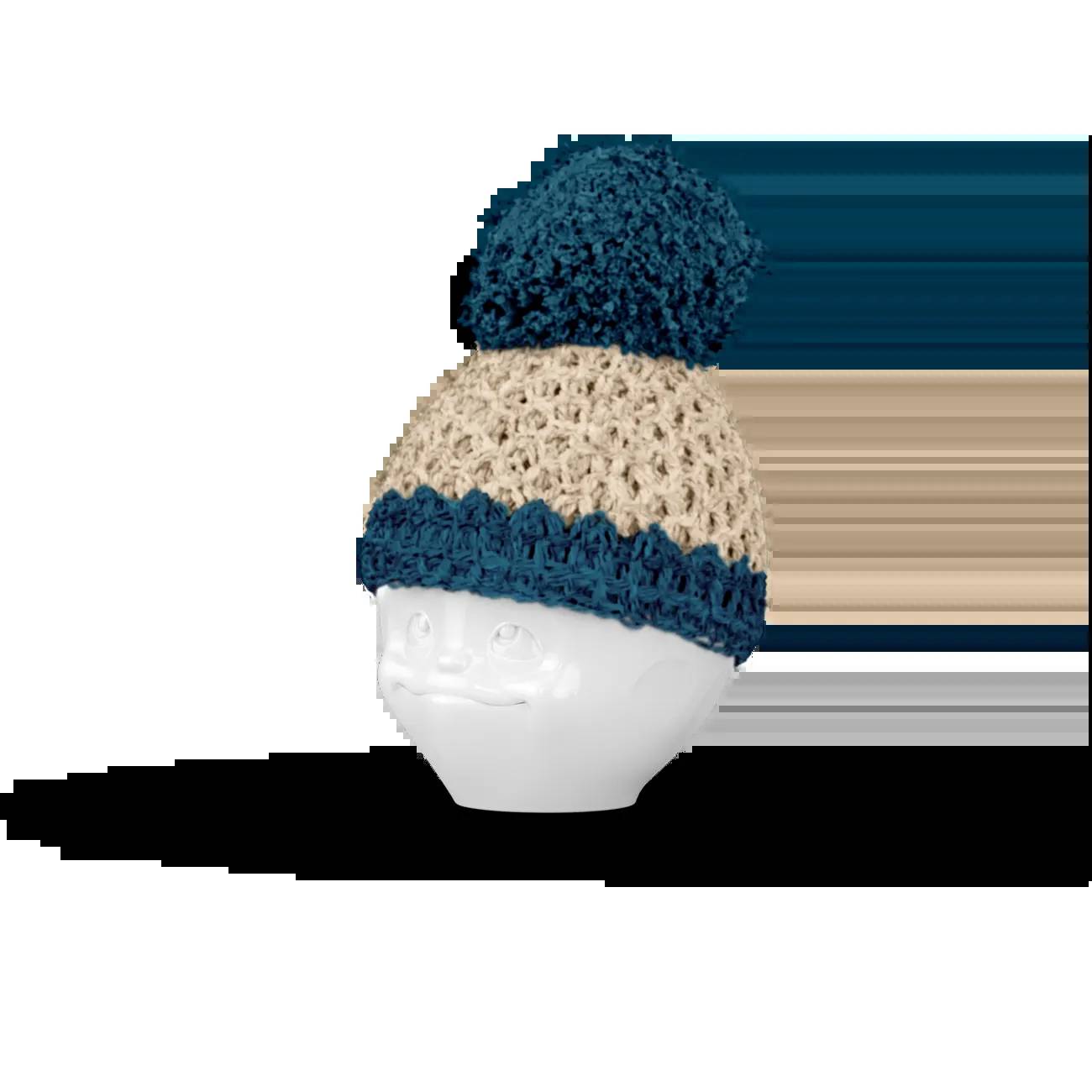 Gehäkelte Creme- und Blau-Strickmütze mit Pompon auf einem weißen Schaufensterkopf vor schwarzem Hintergrund.