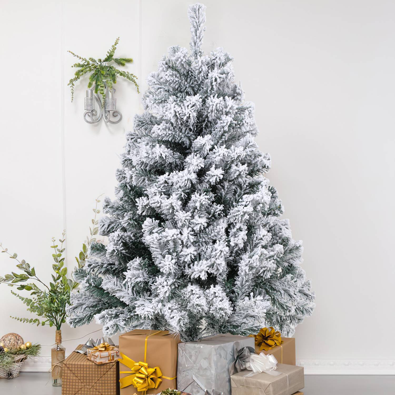 Schneebedeckter künstlicher Weihnachtsbaum mit eingepackten Geschenken an seiner Basis in einem hellen Raum.