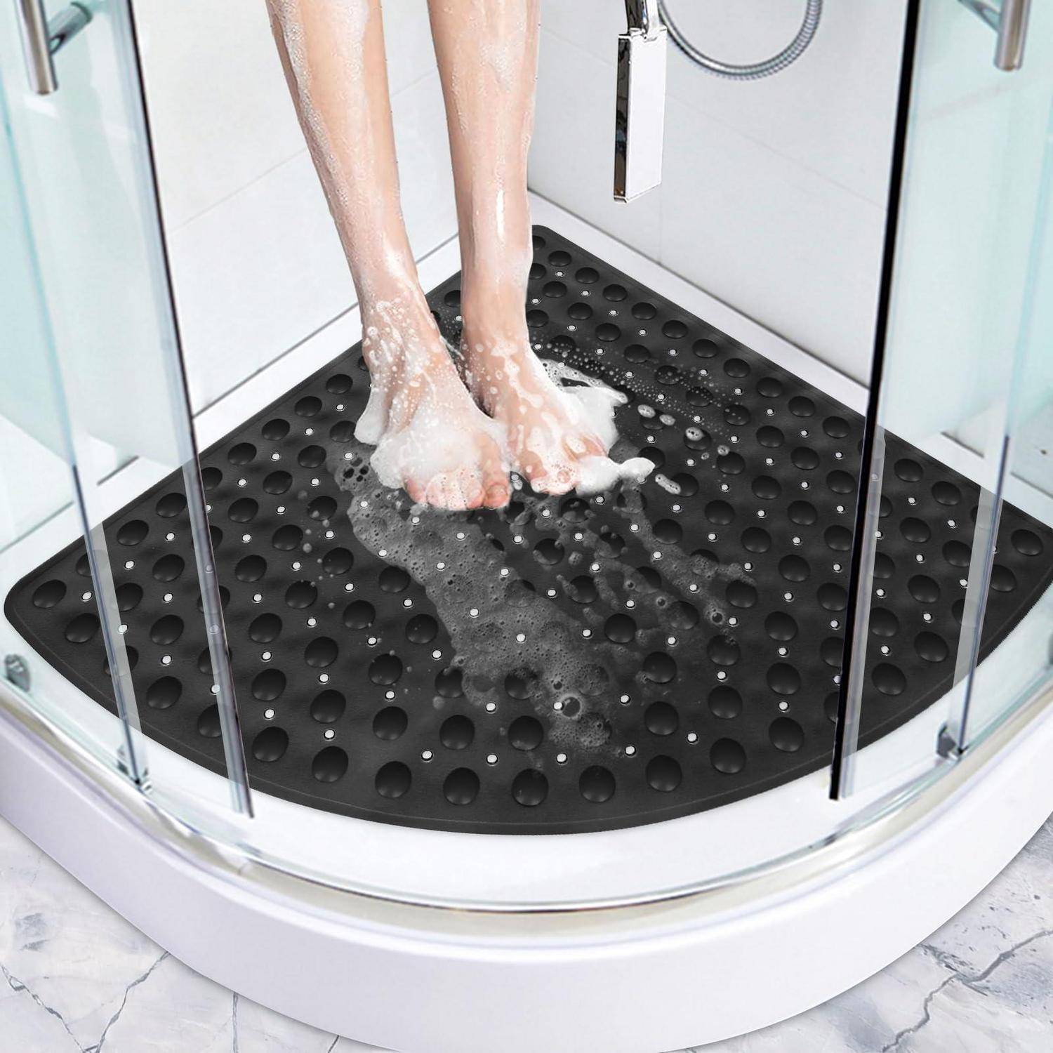 Person, die Füße in einer Dusche auf einer schwarzen rutschfesten Gummimatte in einer Glasduschkabine wäscht.