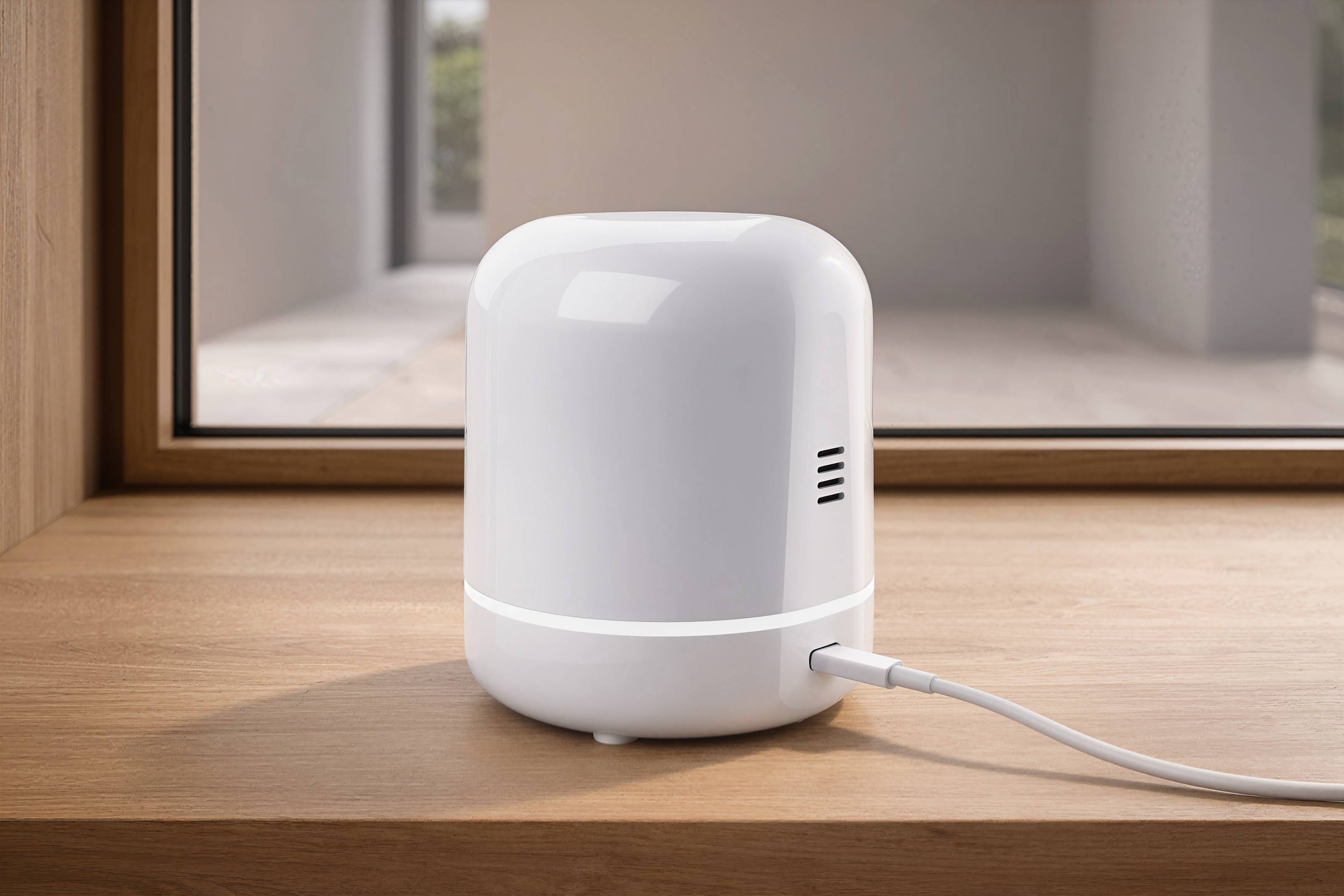Ein kleines weißes zylindrisches intelligentes Gerät sitzt auf einem Holztisch, mit einem Kabel angeschlossen, in einem modernen Raum.
