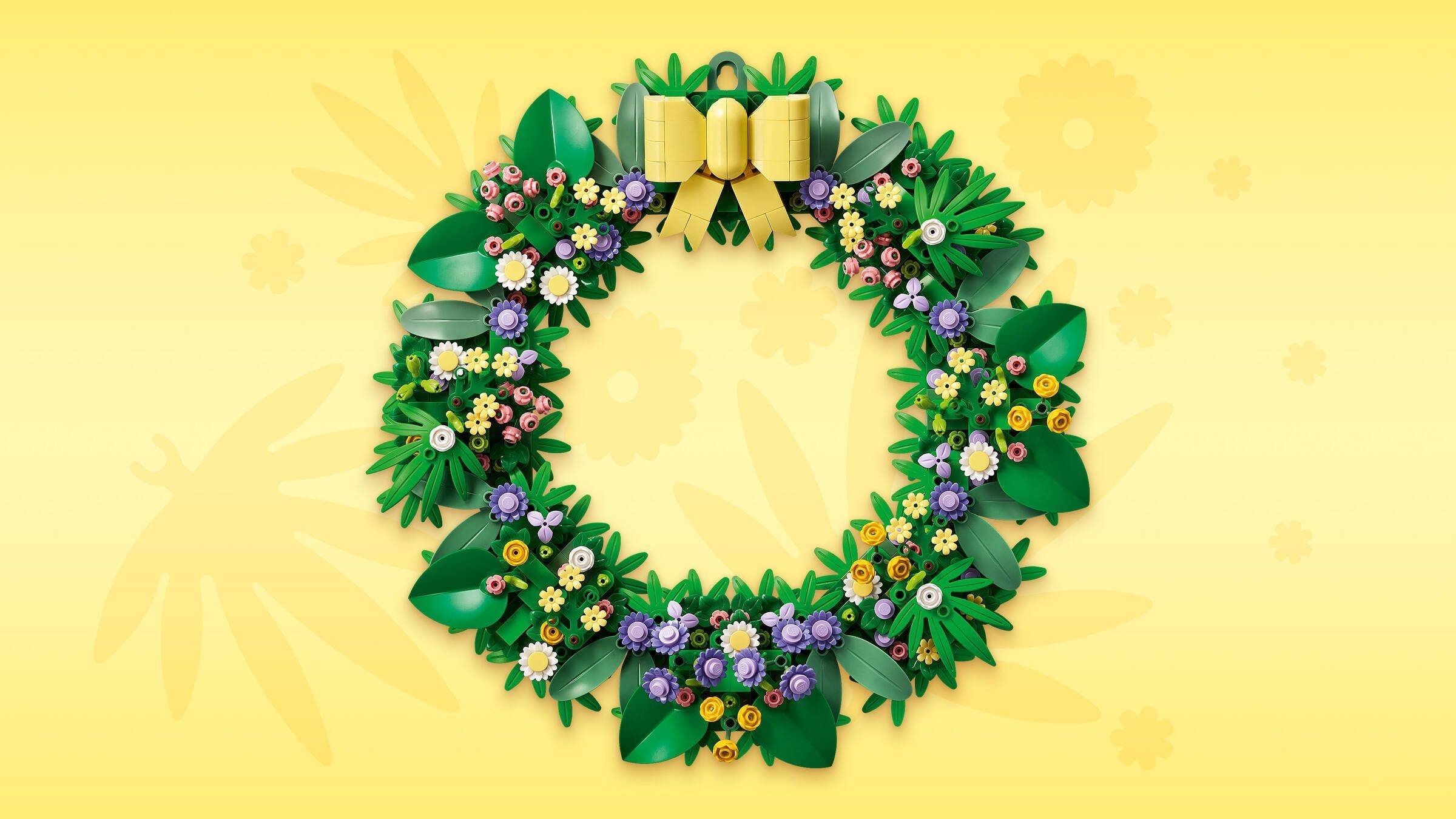 Ein dekoratives Blumenkranz mit grünen Blättern, violetten und gelben Blüten und einer goldenen Schleife auf einem sanften gelblichen Hintergrund.