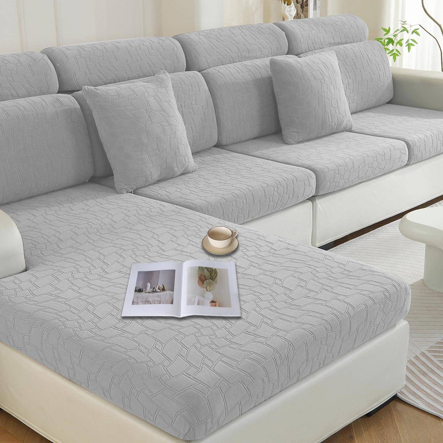 Graues Ecksofa mit angepasstem strukturiertem Sofabezug und passenden Kissen, gezeigt in einem hellen Wohnzimmer mit einer offenen Zeitschrift und einer Tasse auf der Récamière.