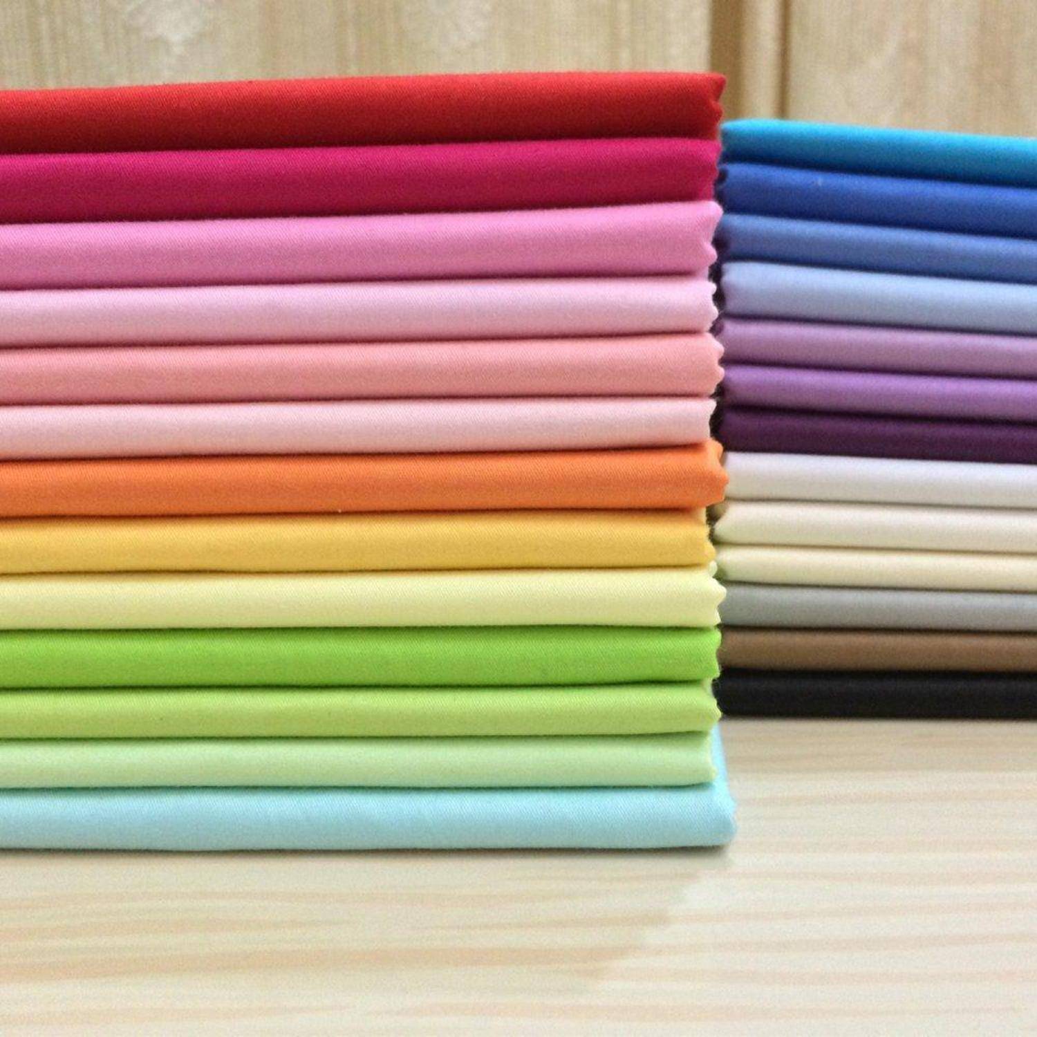 Stapel von ordentlich gefalteten Stoffen oder Handtüchern in einem Regenbogen von Farben, angeordnet in zwei Stapeln auf einer hellen Holzoberfläche.