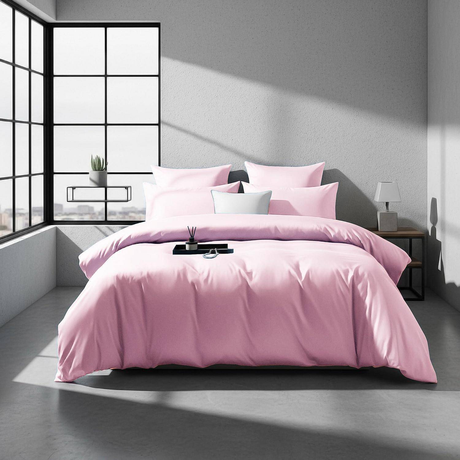 Modernes Schlafzimmer mit einer rosa Bettdecke und Kissen, sonnendurchflutet neben großen schwarzgerahmten Fenstern in einem minimalistischen grauen Raum.
