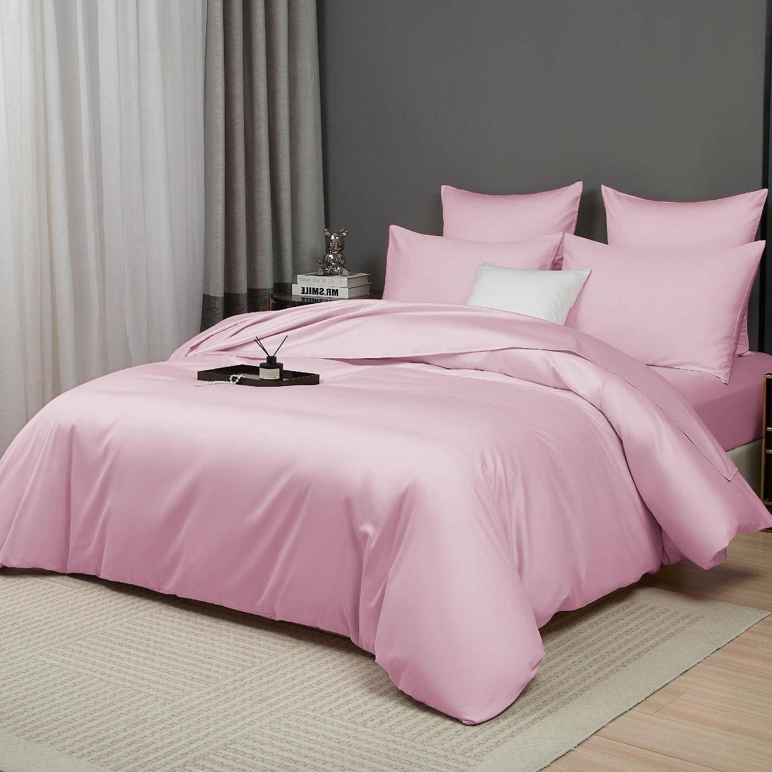 Ein Bett mit rosa Bettwäsche und Kissen, einschließlich eines weißen Akzentkissens, in einem ordentlichen Schlafzimmer mit Vorhängen und einem Teppich.