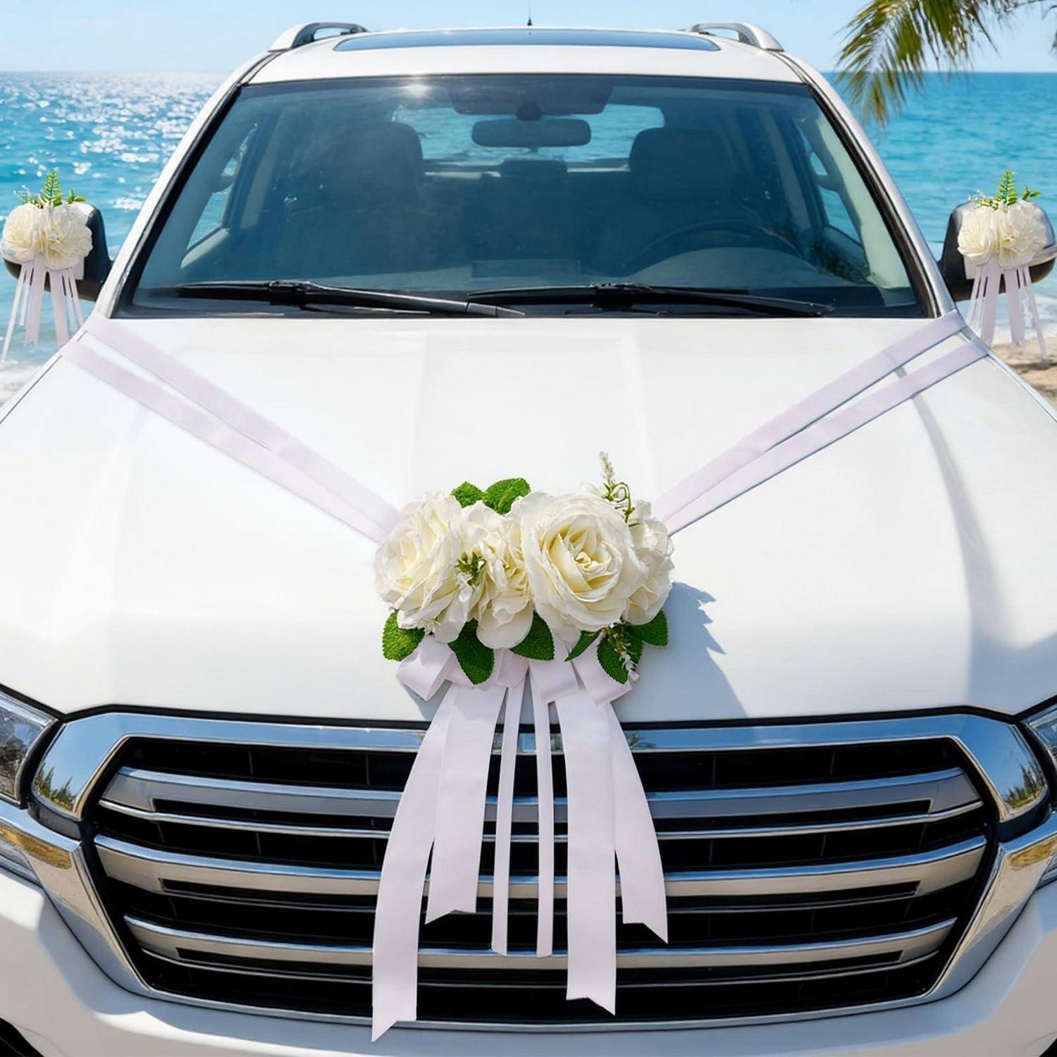 Weißes Hochzeitsauto mit weißen Blumen und Bändern geschmückt, geparkt an einem Strand mit Ozean und Palmen im Hintergrund.