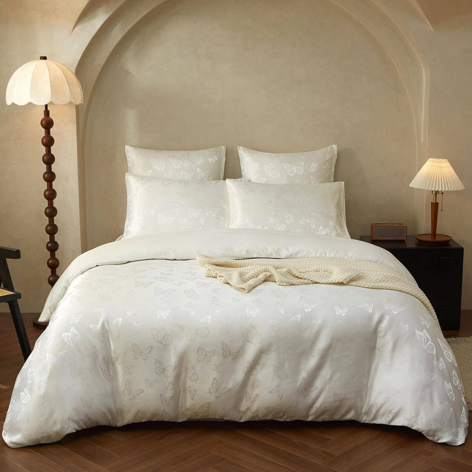 Ein ordentlich gemachtes Bett mit weißer Bettwäsche und Kissen in einem minimalistischen beigefarbenen Schlafzimmer, flankiert von zwei Nachttischlampen.