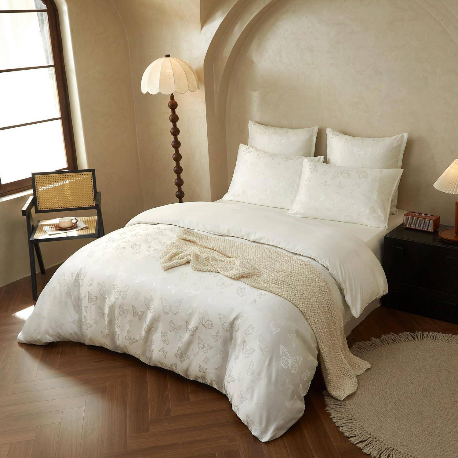 Gemütliches Schlafzimmer mit einem sorgfältig gemachten weißen Bett, Stehlampe, Nachttischen und Fensterstuhl in einem warmen beigefarbenen Interieur.