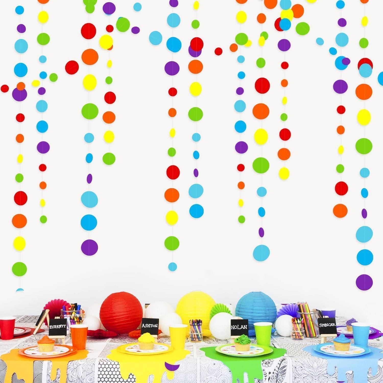 Bunte Papiergirlanden mit Punkten hängen über einem dekorierten Partytisch mit leuchtenden Laternen, Bechern, Tellern und Geburtstagsleckereien.