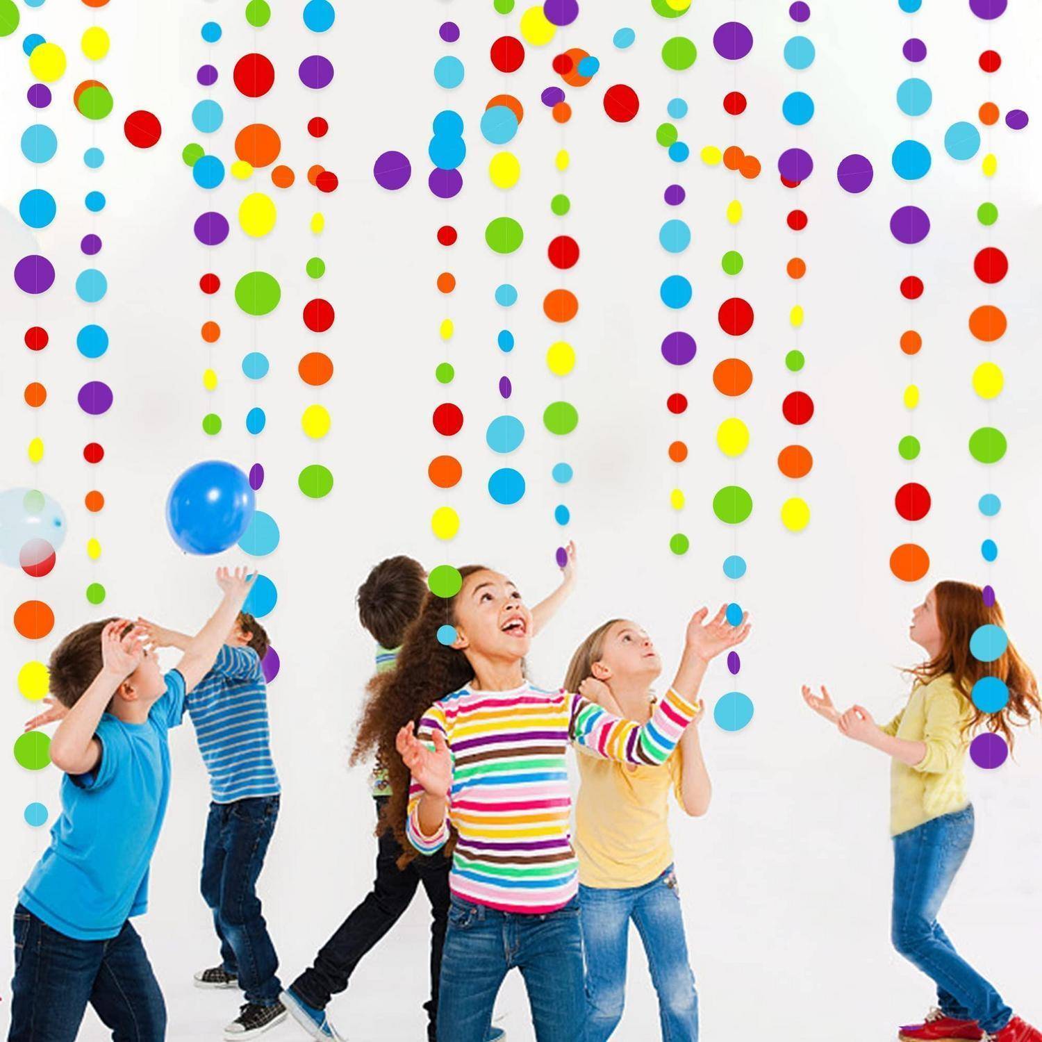 Kinder spielen und greifen nach bunten hängenden Papierpunkten mit Ballons in einer hellen Indoor-Partyatmosphäre.