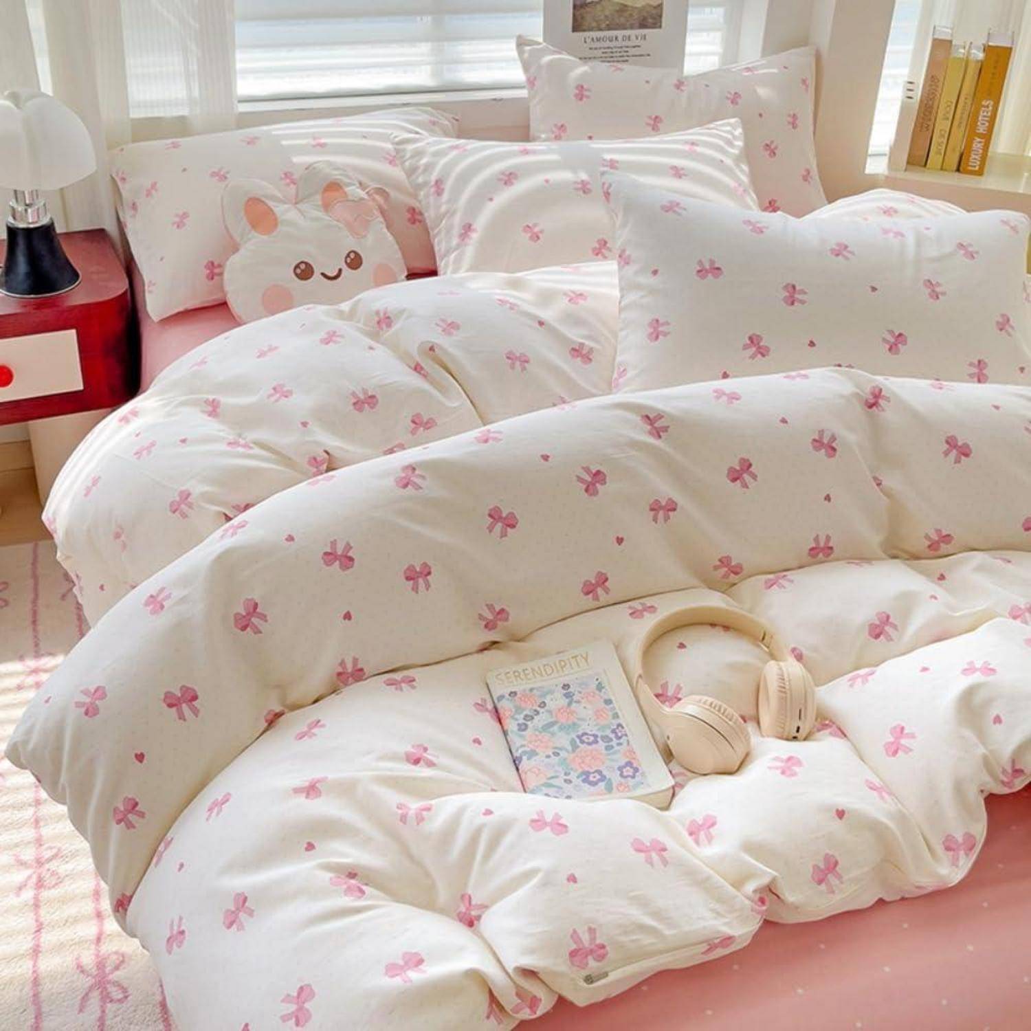 Rosa und weiße Schlafzimmerbettwäsche mit kleinem Blumenmuster, ein Kissen mit Mausgesicht und ein Buch mit Kopfhörern auf dem Bett.
