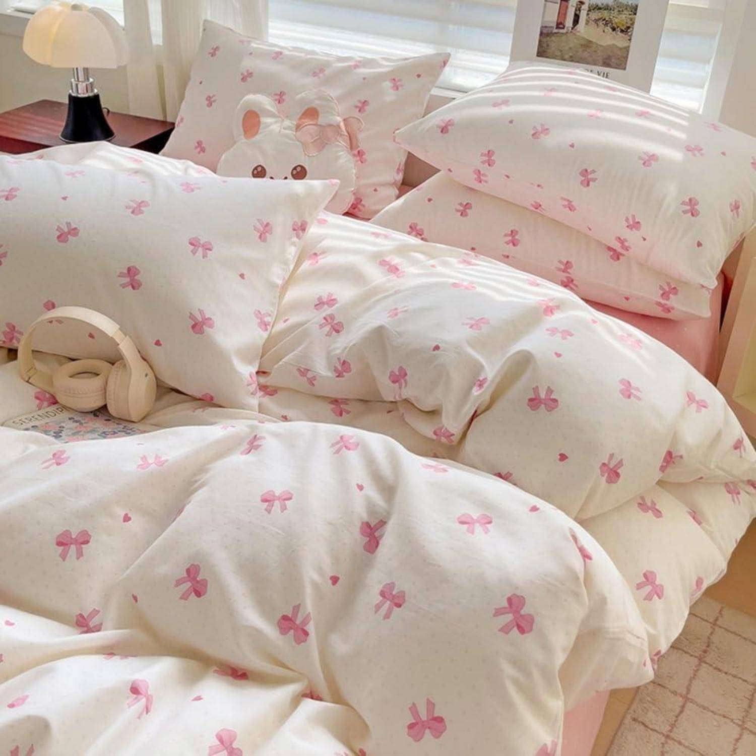 Ein ordentlich gemachtes Bett mit cremefarbener Bettwäsche mit rosafarbenen Schleifendruck, einem passenden Häschenkissen und Kopfhörern, die auf der Decke ruhen.
