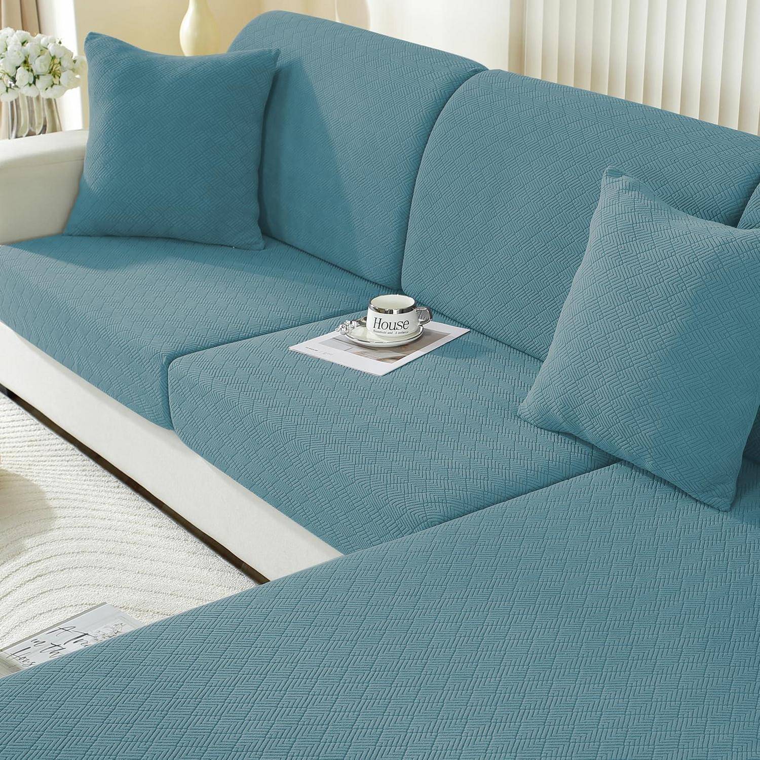 Blaues Ecksofa mit strukturiertem Schonbezug und passenden Kissen, gezeigt in einem hellen Wohnzimmer mit einer Kaffeetasse auf einer Zeitschrift.