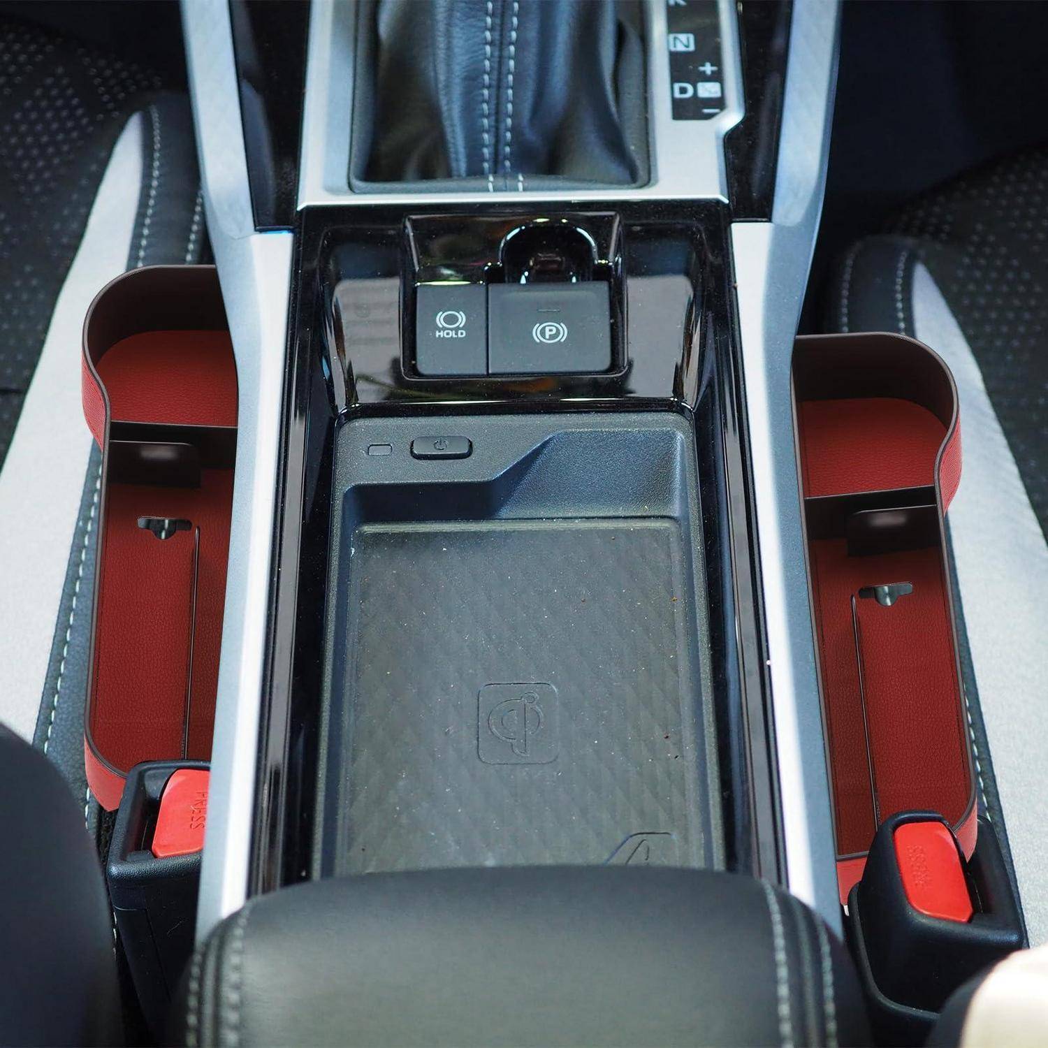 Mittelkonsole des Autos mit Schalthebel, elektronischer Feststellbremse und zwei offenen Staufächern mit roten Rändern auf beiden Seiten.