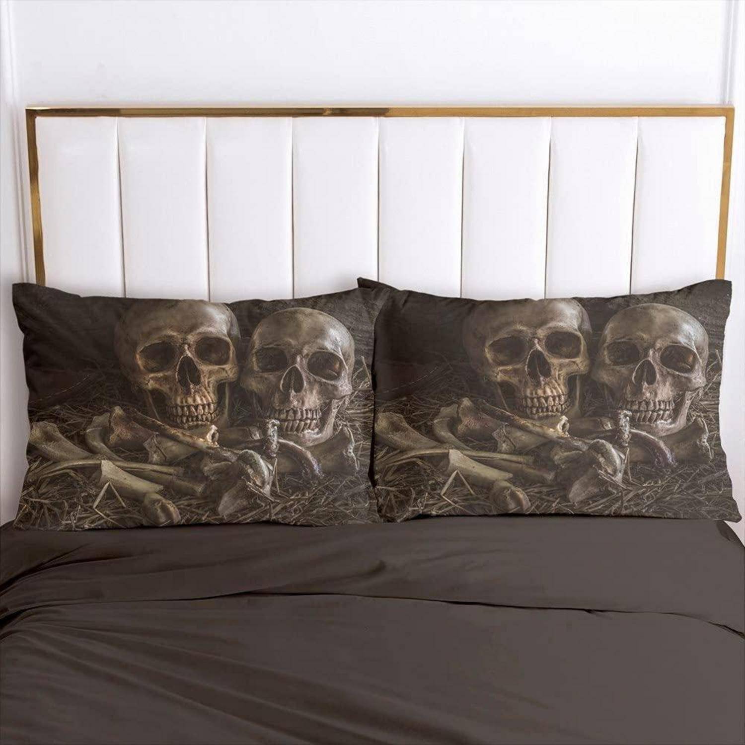 Bett mit zwei Kissen mit Totenkopf-Druck gegen ein weiß gepolstertes Kopfteil und dunkle Bettwäsche.