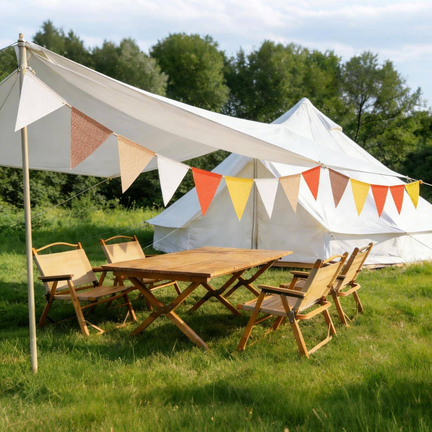 Outdoor-Glamping-Bereich mit einem großen weißen Zelt, einem Vordach, Wimpelketten und einem Holztisch mit Klappstühlen auf Gras.