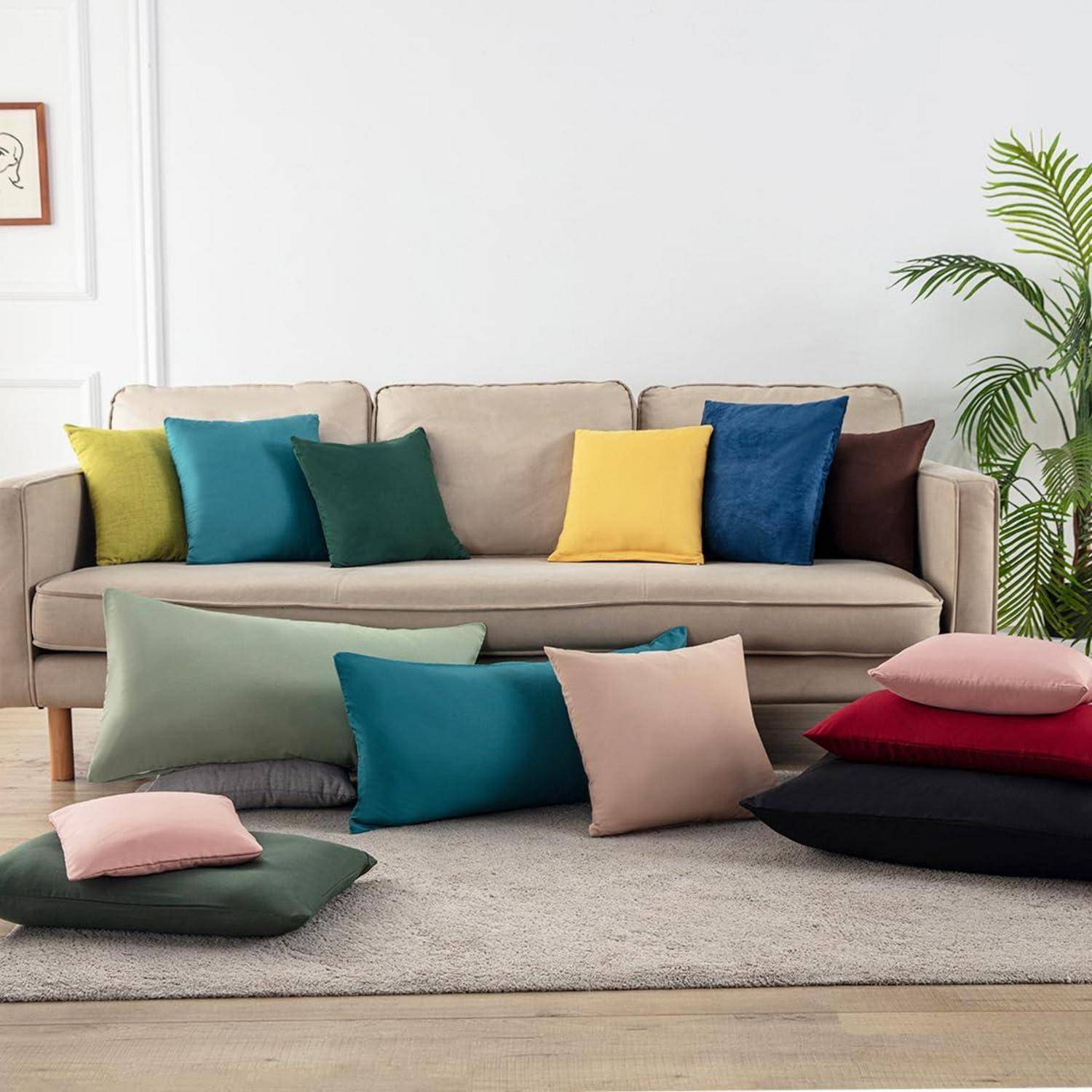 Beige Sofa mit farbenfrohen Dekokissen und gestapelten Bodenkissen in einem minimalistischen Wohnzimmer, was eine entspannte, aufeinander abgestimmte Sitzplatzanordnung suggeriert.