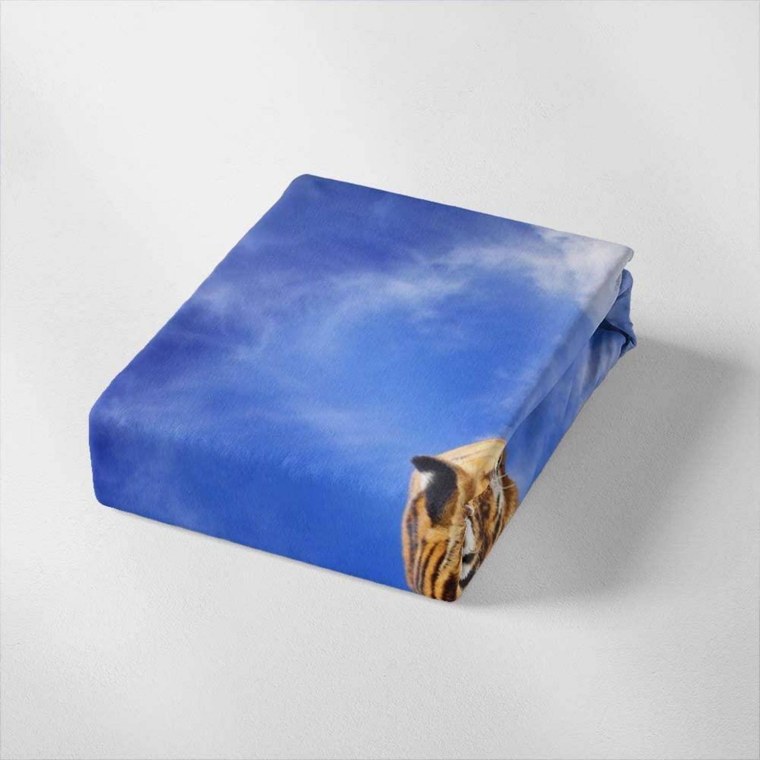 Blaugleiches gefaltetes Tuch oder Beutel mit Himmelsdruck und einem Tigerkopf, der aus einer Ecke hervorlugt, auf weißem Hintergrund.