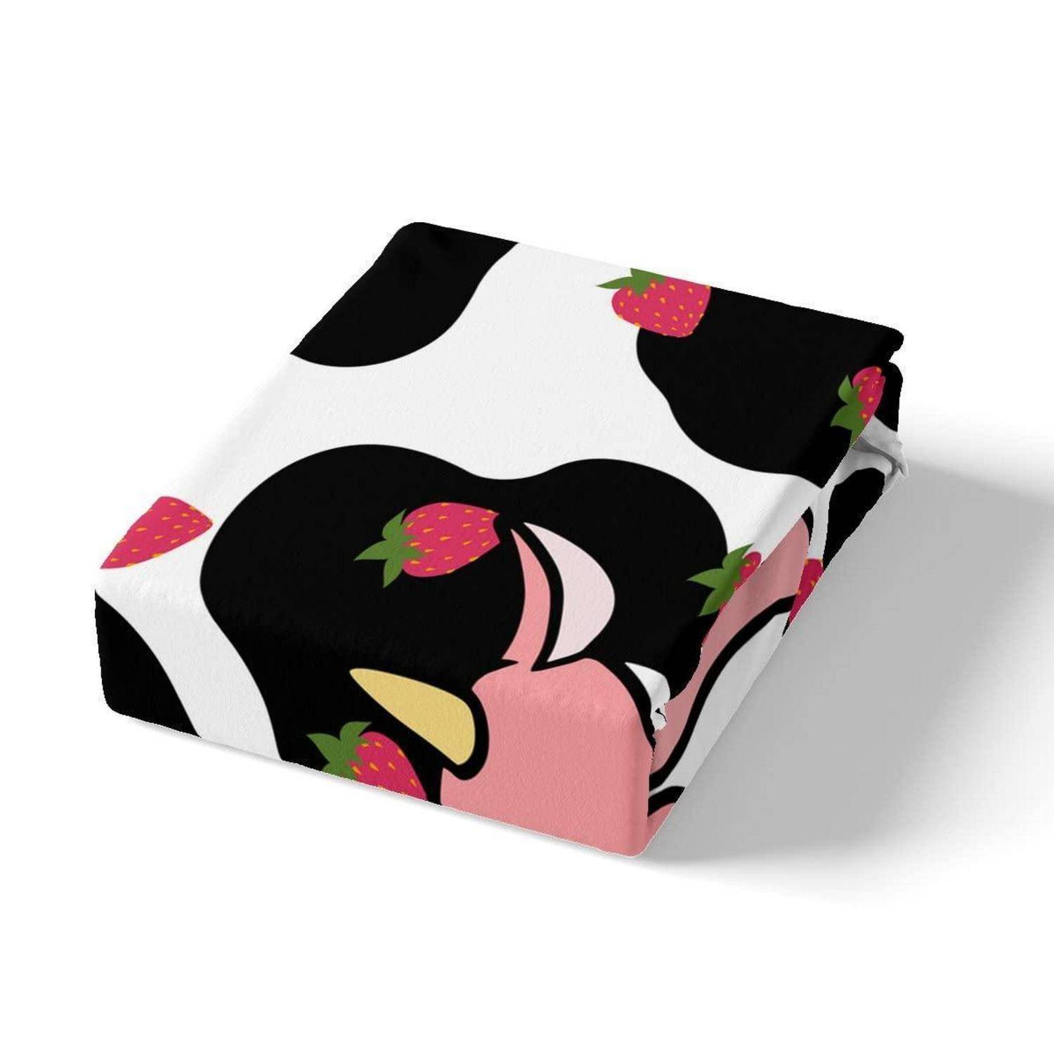 Ein gefalteter Stoff mit einem Schwarz-Weiß-Kuh-Muster, akzentuiert durch rosa Erdbeeren und ein rosa Cartoon-Gesichtsdesign.