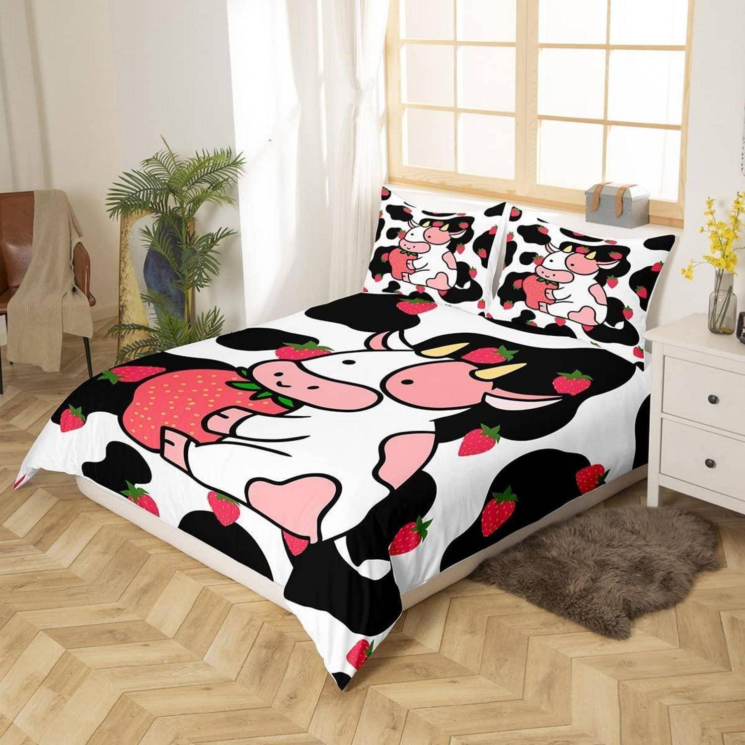 Bettwäsche-Set mit Kuh-Motiven, rosa Cartoon-Kühe und Erdbeeren auf einem schwarz-weißen Bett in einem hellen Schlafzimmer.