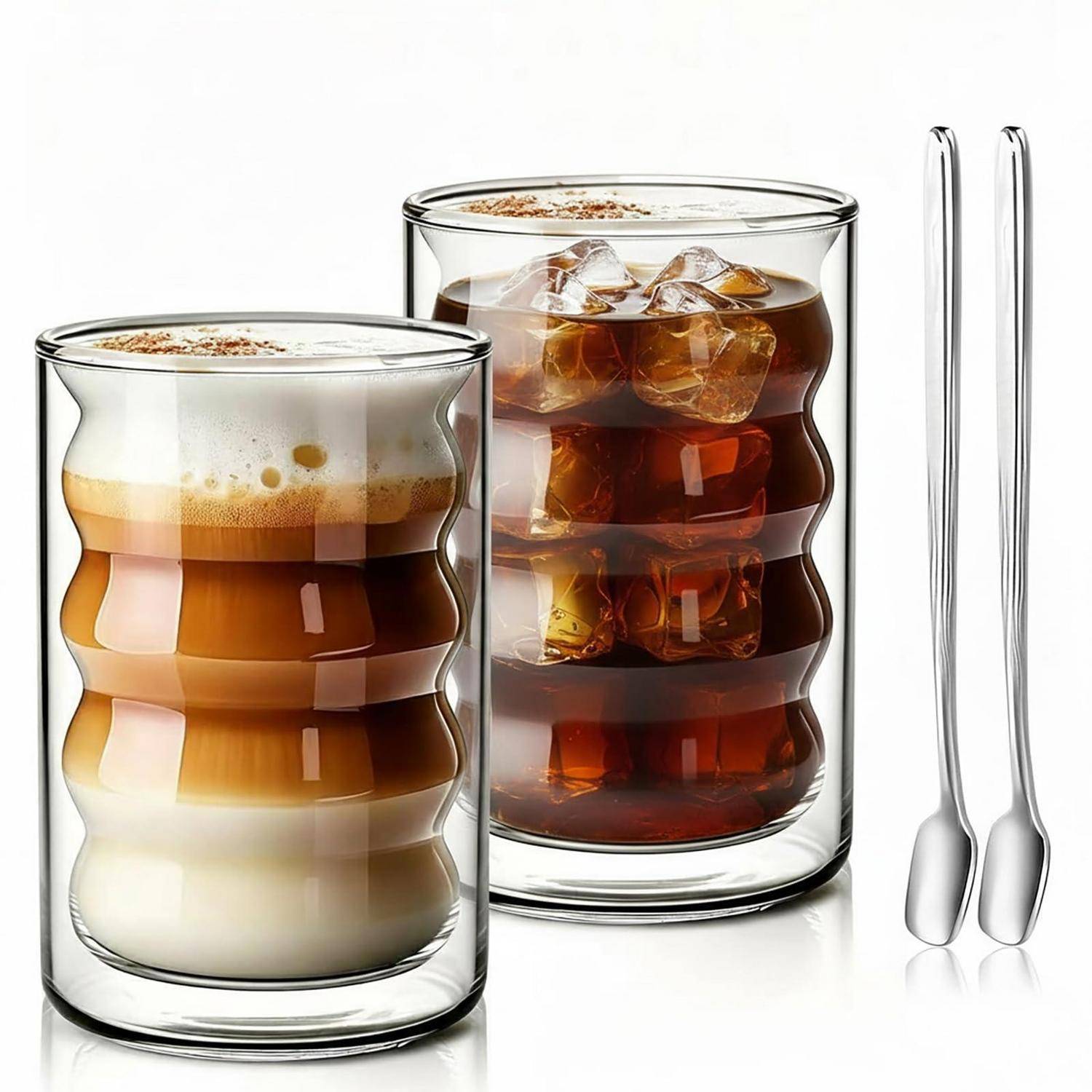 Zwei geschichtete Eiskaffee-Getränke in klaren Gläsern, eines mit Milch und Schaum und eines schwarz über Eis, neben zwei langen Löffeln.