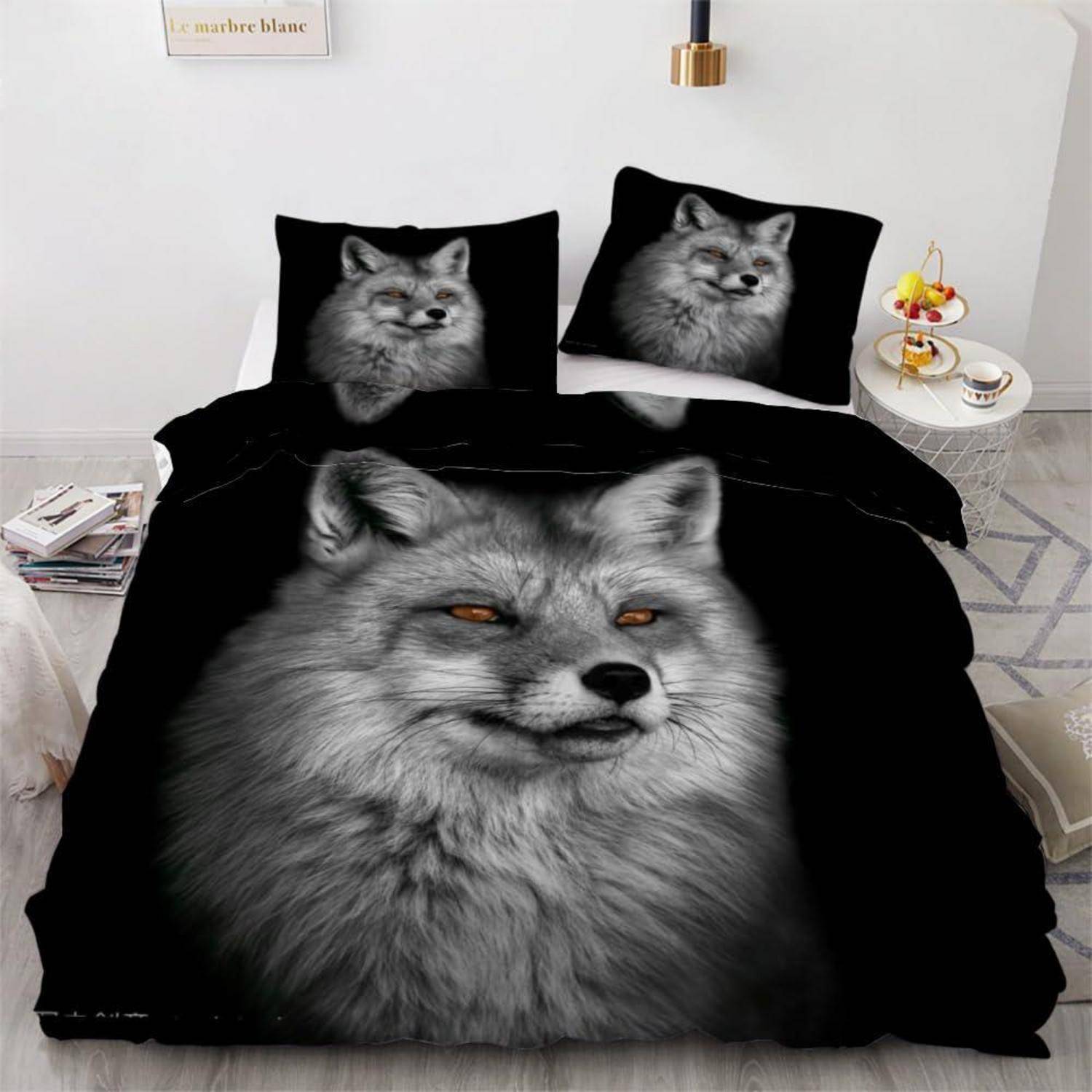 Bett mit schwarzer Bettwäsche bedruckt mit einem großen grauen Fuchsgesicht; passende Kissen mit Fuchsgesicht und ein kleiner Nachttisch mit Tee und Obst.