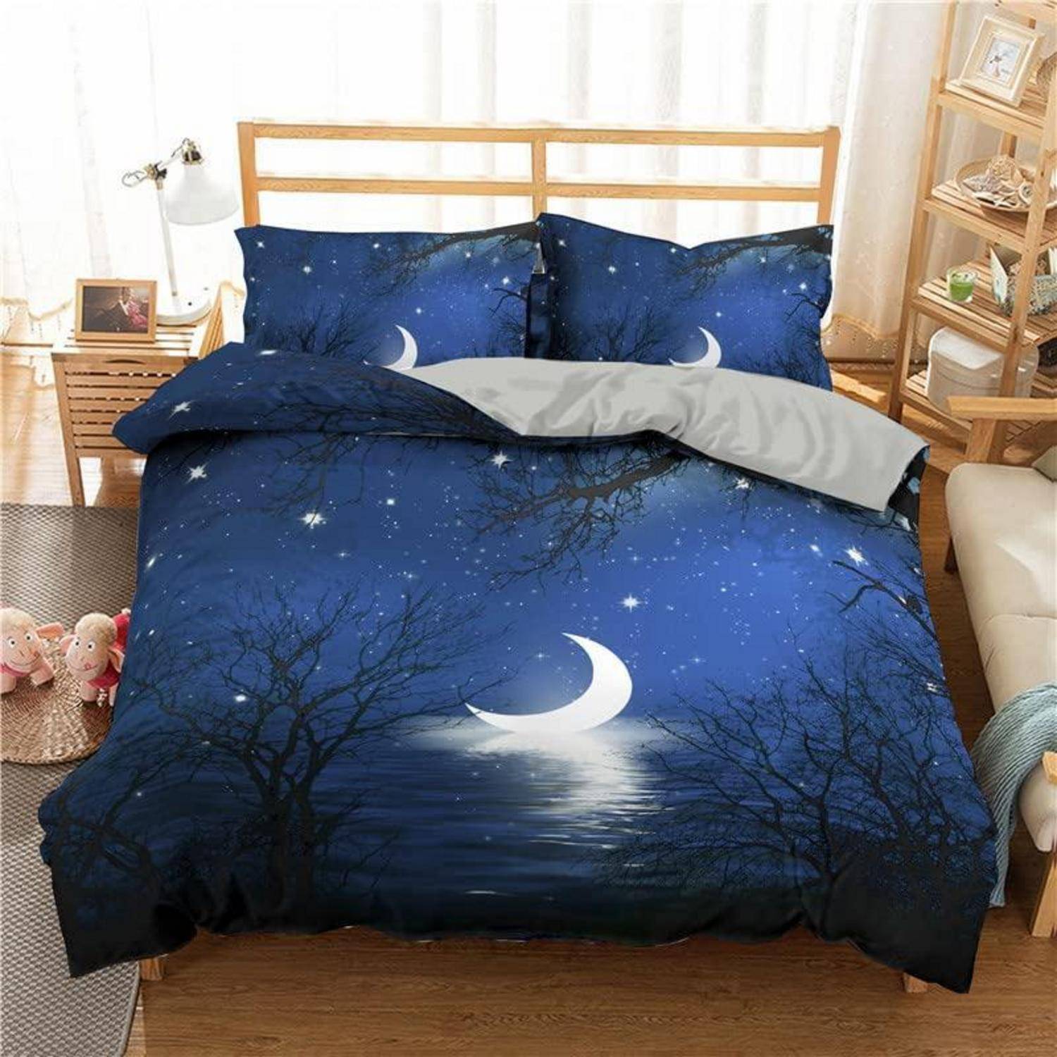 Ein ordentlich gemachtes Bett mit dunkelblauer Bettwäsche mit Mond- und Sternenmotiven, weißen Mondsicheln und Baumsilhouetten in einem hellen Schlafzimmer.