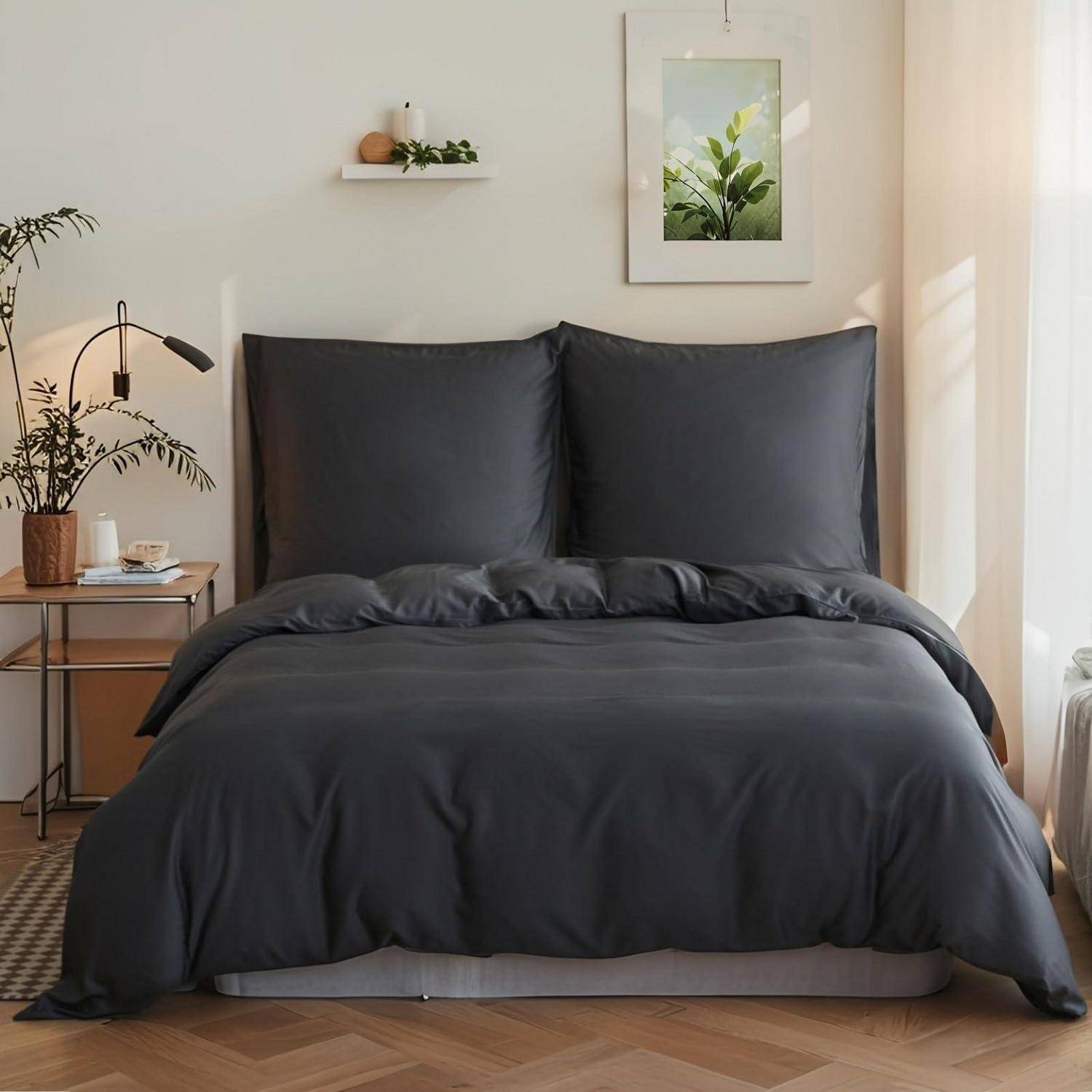 Ordentlich gemachtes Bett mit dunkelgrauer Bettwäsche in einem minimalistischen Schlafzimmer neben einem kleinen Nachttisch, einer Lampe, einer Pflanze und einem gerahmten Wandbild.