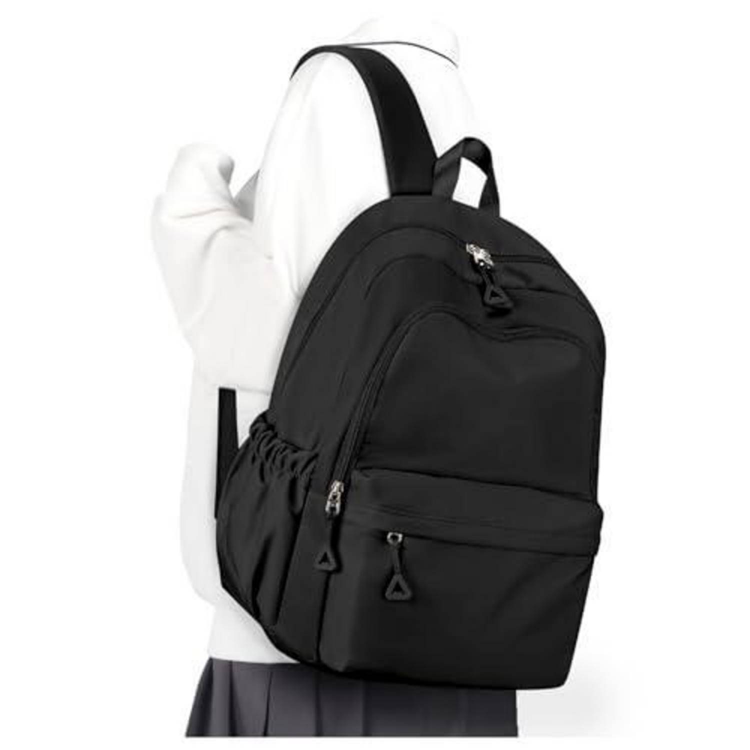 Schwarzer Rucksack, über eine Schulter getragen, von einer Person in einem weißen Oberteil, vor einem einfachen weißen Hintergrund gezeigt.