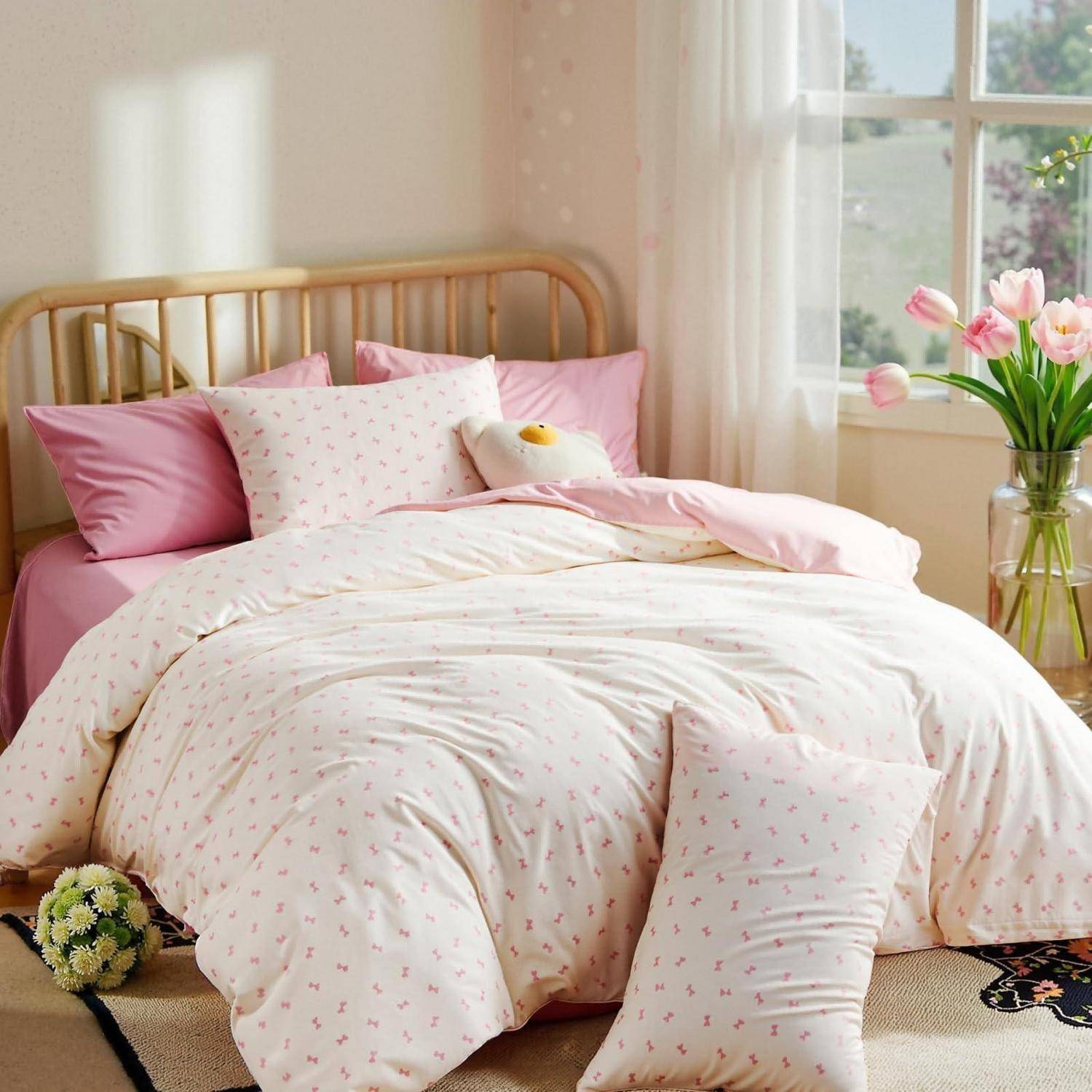 Rosarot und weiß gestreuertes Bett mit floralem Steppdecke, Kissen und ein kleines Kuscheltier neben einem Fenster mit Tulpen in einer Vase.