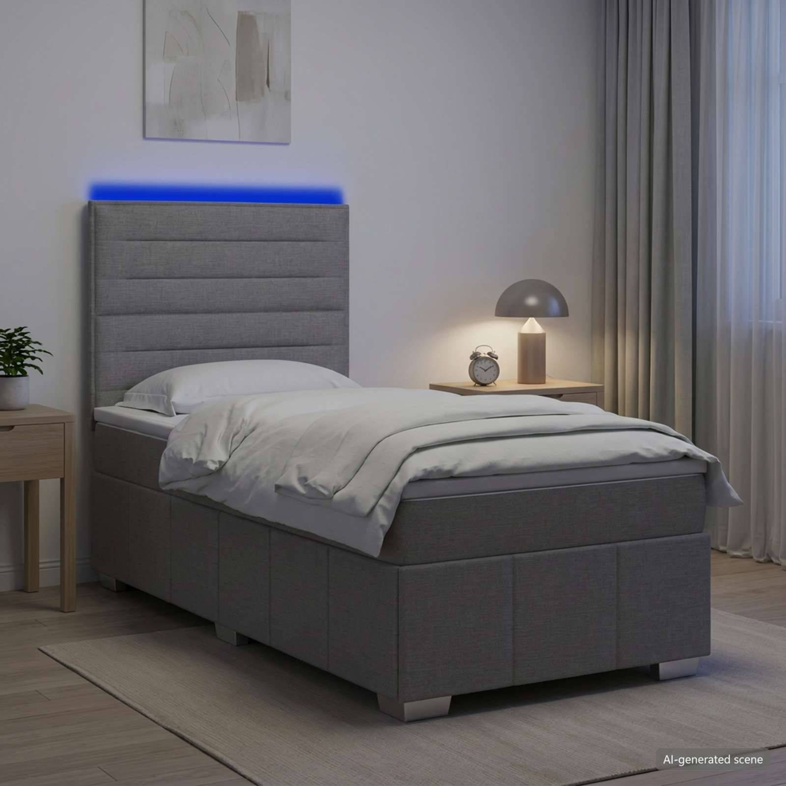 Modernes grau gepolstertes Einzelbett in einem Schlafzimmer mit leuchtender blauer Kopfleuchte, Nachttisch, Lampe und Wecker.