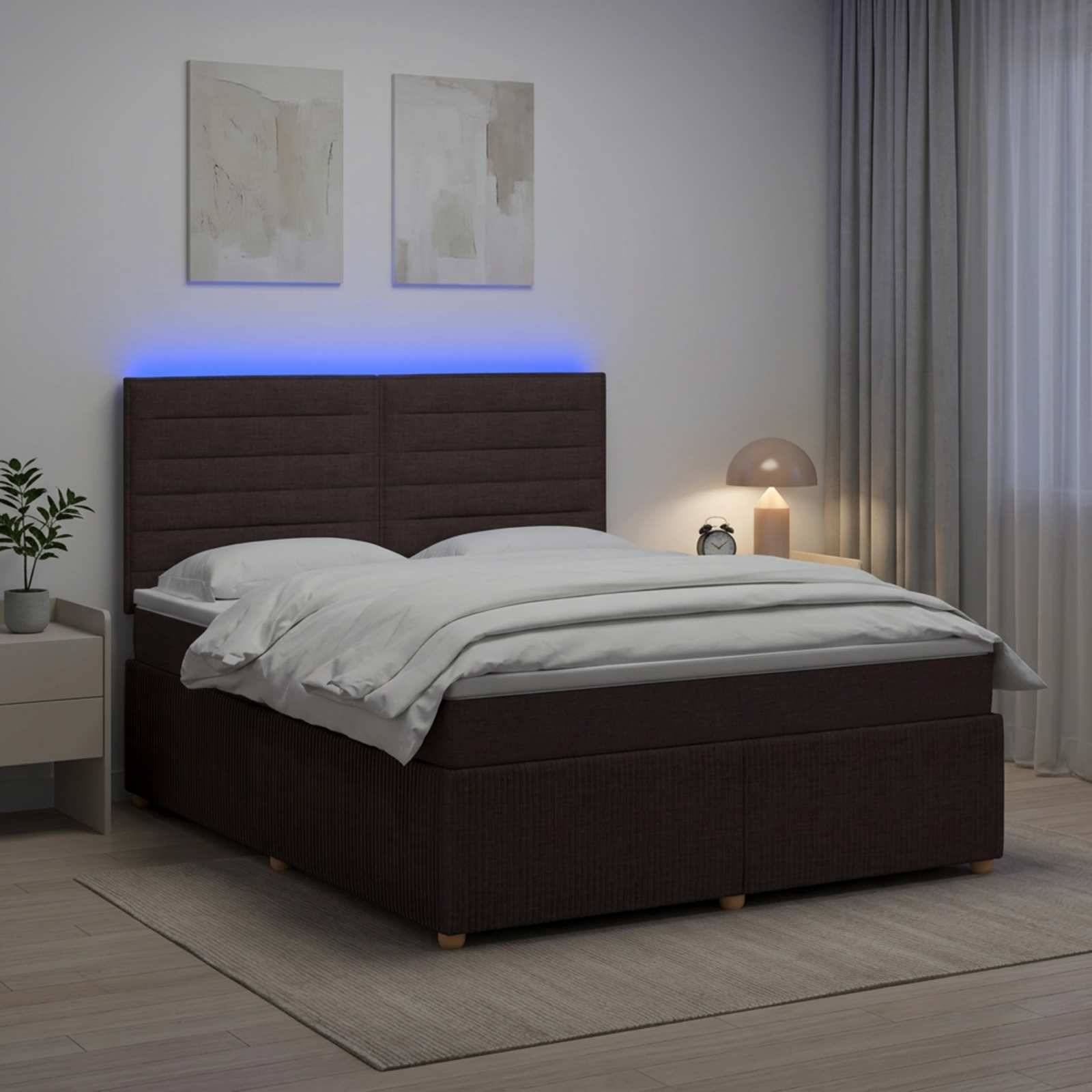 Modernes Schlafzimmer mit dunkel gepolstertem Bett, weißer Bettwäsche, blau beleuchteter Kopfteil, Nachttischlampe, Pflanze und Wandkunst.