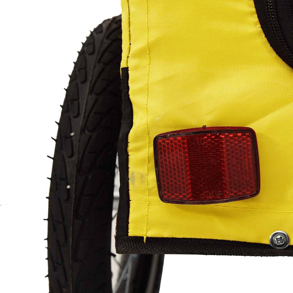 Nahaufnahme eines gelben Fahrradanhängers oder einer gelben Tasche mit einem roten hinteren Reflektor neben einem schwarzen Rad auf weißem Hintergrund.