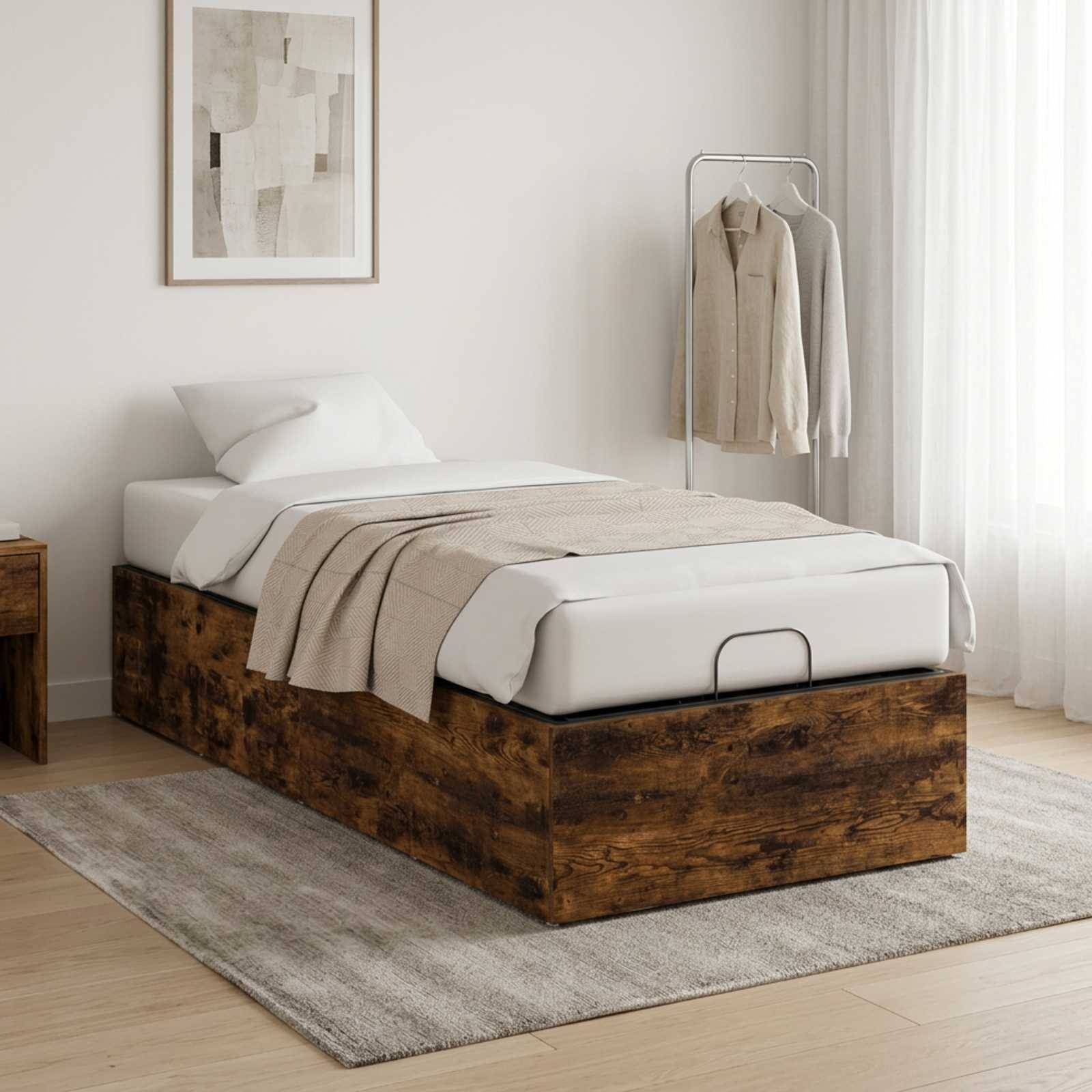 Minimales Schlafzimmer mit einem Einzelbett auf einer rustikalen Holzlagerungsbasis, weißer Bettwäsche, beige Wurfdecke, gerahmter Wandkunst und einem Kleiderständer neben durchsichtigen Vorhängen.