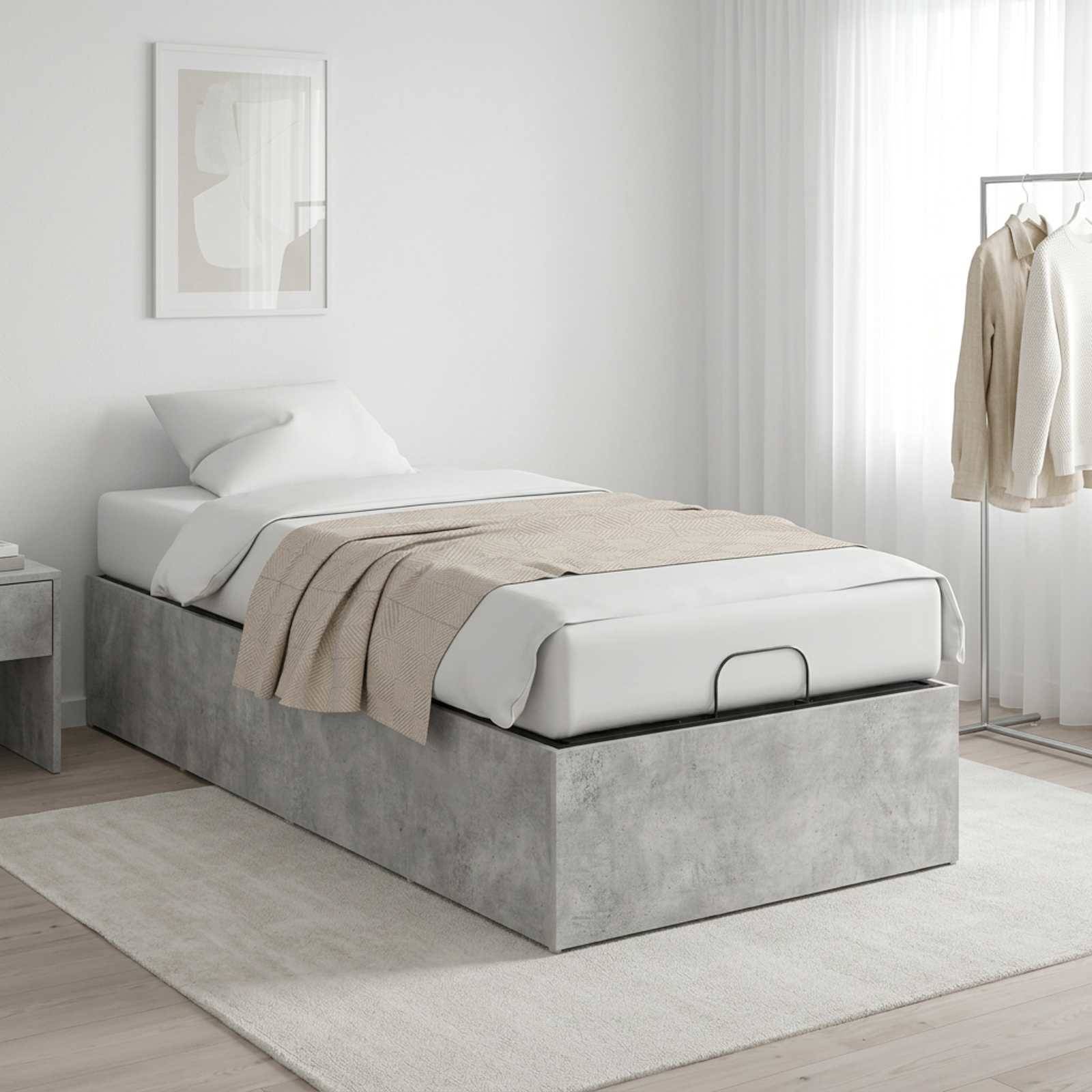Minimalistisches Schlafzimmer mit einem ordentlich gemachten Einzelbett auf grauer gepolsterter Speicherbasis, beigem Wurf und Kleiderstange neben einem hellen Fenster.