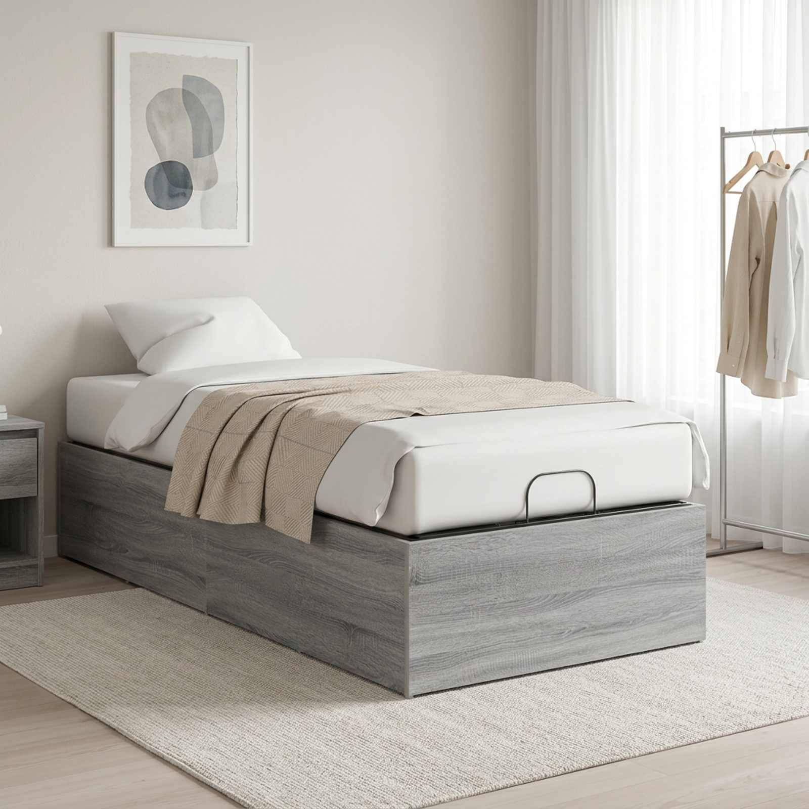 Minimales Schlafzimmer mit einem Einzelbett auf einer Speicherbasis, beigefarbende Bettwäsche, Wandkunst, Nachttisch, Teppich, transparente Vorhänge und ein Kleiderständer.