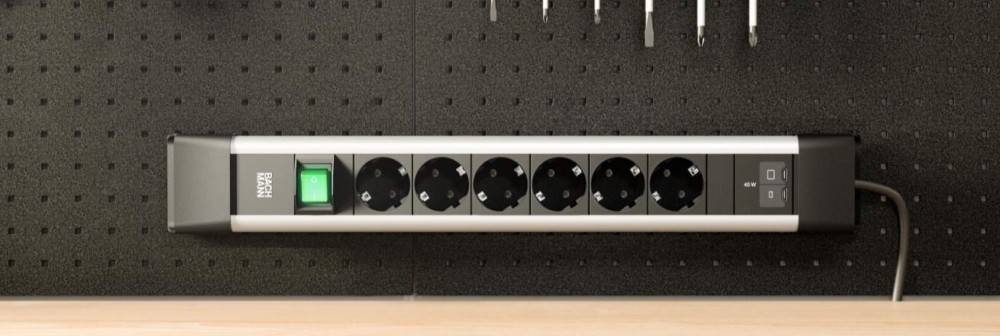 Wandmontierte Steckdosenleiste mit beleuchtetem grünem Hauptschalter und mehreren Steckdosen, ein Stecker auf der rechten Seite angeschlossen.