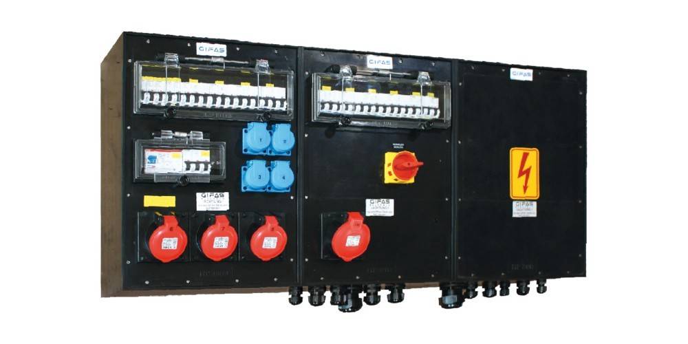 Industrielles Elektrosteuerfeld mit Schaltern, blauen Steckdosen, roten Buchsen und einem gelben Hochspannungswarnschild.
