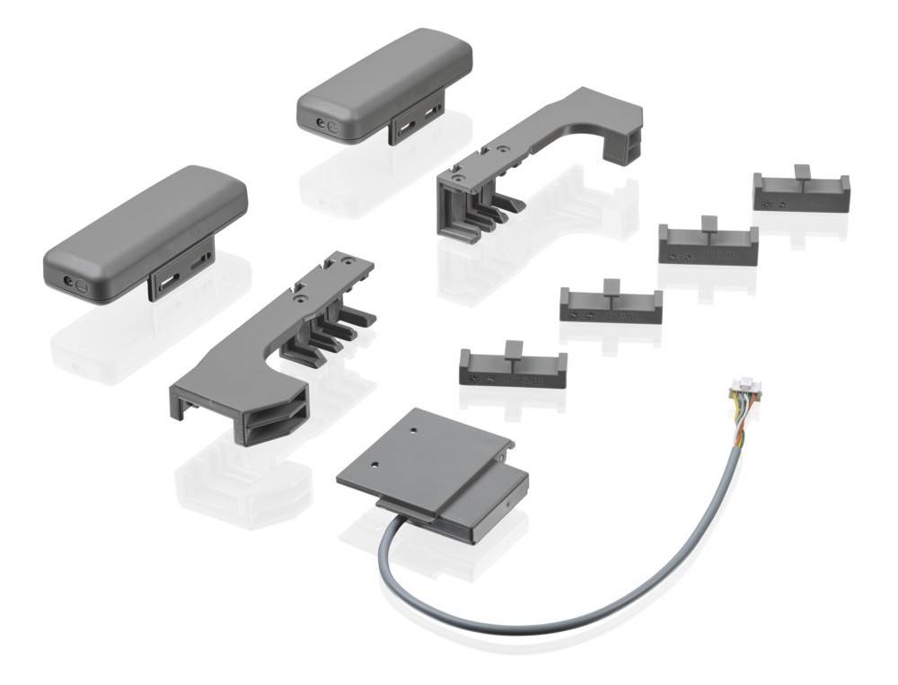 Explosionszeichnung einer modularen grauen elektronischen Steckverbinderanordnung mit Gehäuseteilen, Befestigungswinkeln, Klammern und einem mehrfarbigen Kabelstrang.
