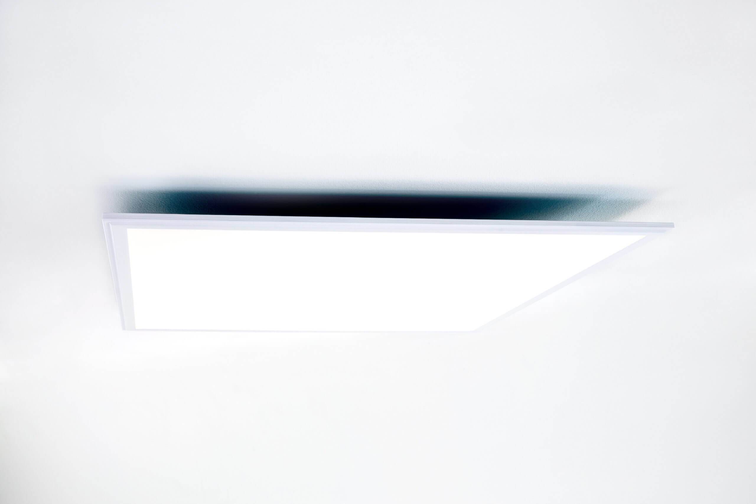 Ein minimalistisches weißes rechteckiges Lichtpaneel oder eine Deckenleuchte mit einem dunklen unscharfen Spiegelbild oder Schatten darüber.