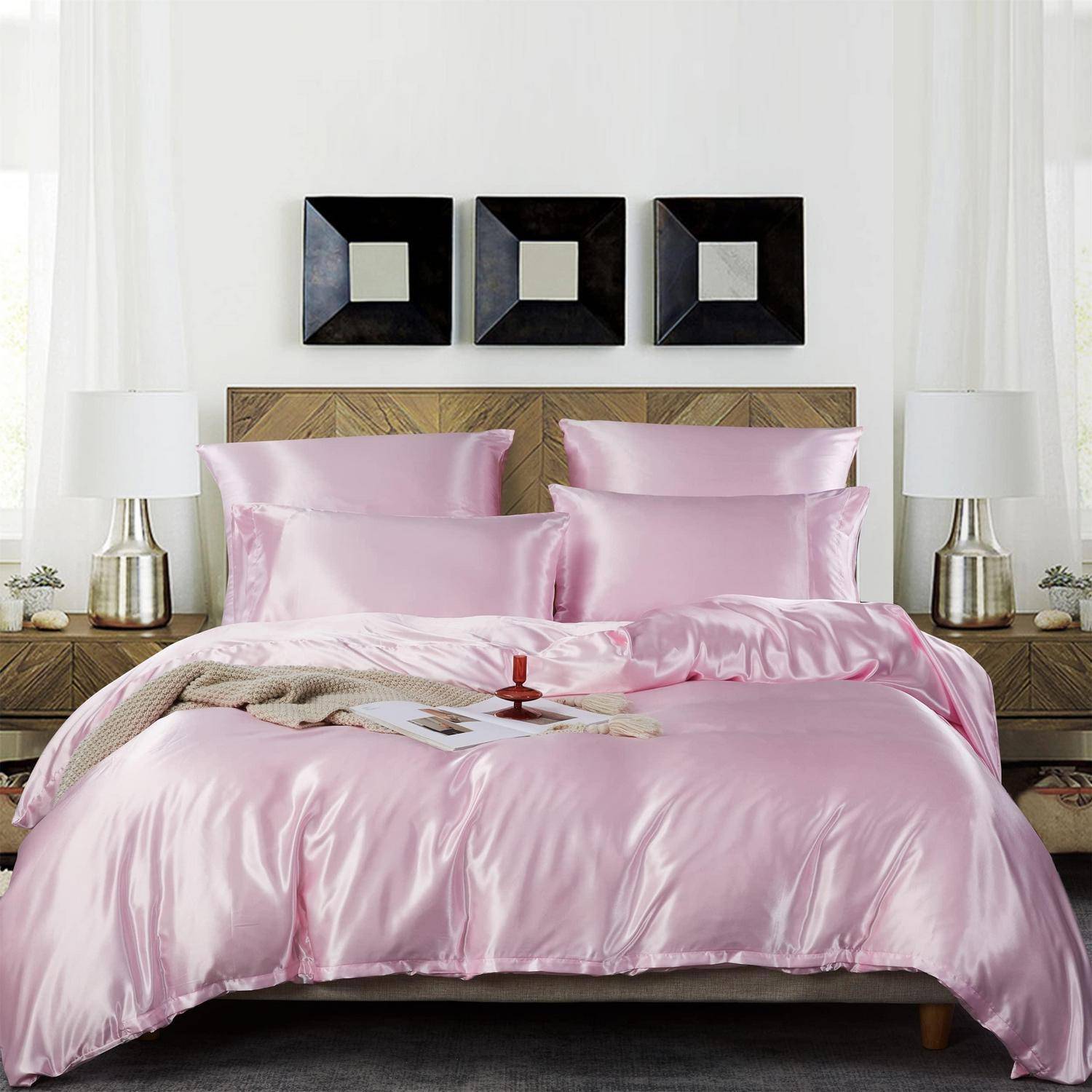 Rosa Satinbettwäsche auf einem ordentlich gemachten Bett mit gemustertem Kopfteil, flankiert von Nachttischlampen und drei schwarzen quadratischen Wandspiegeln in einem modernen Schlafzimmer.