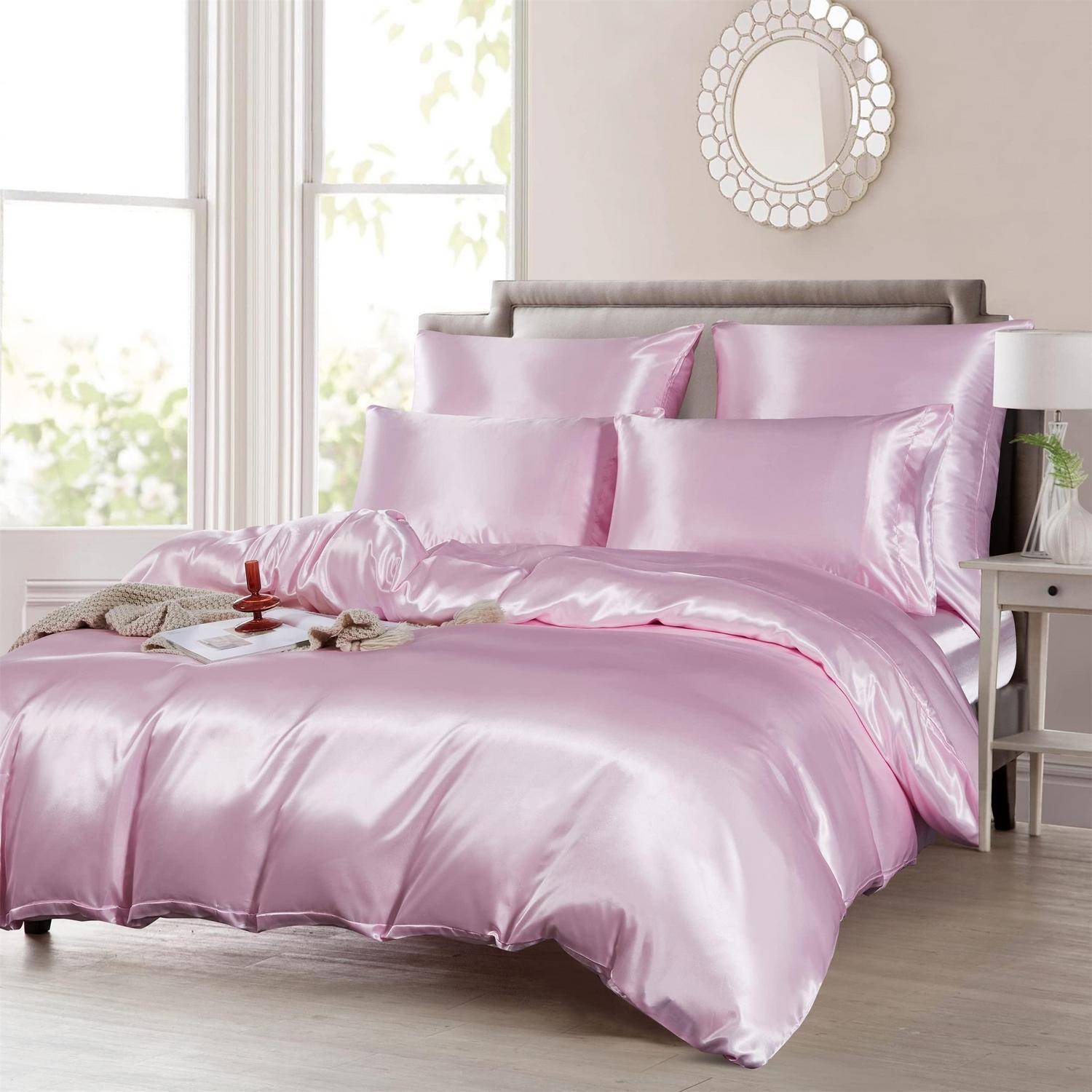 Rosa Satinbettwäsche auf einem ordentlich gemachten Bett in einem hellen Schlafzimmer, mit passenden Kissen, Bettdecke und Laken.